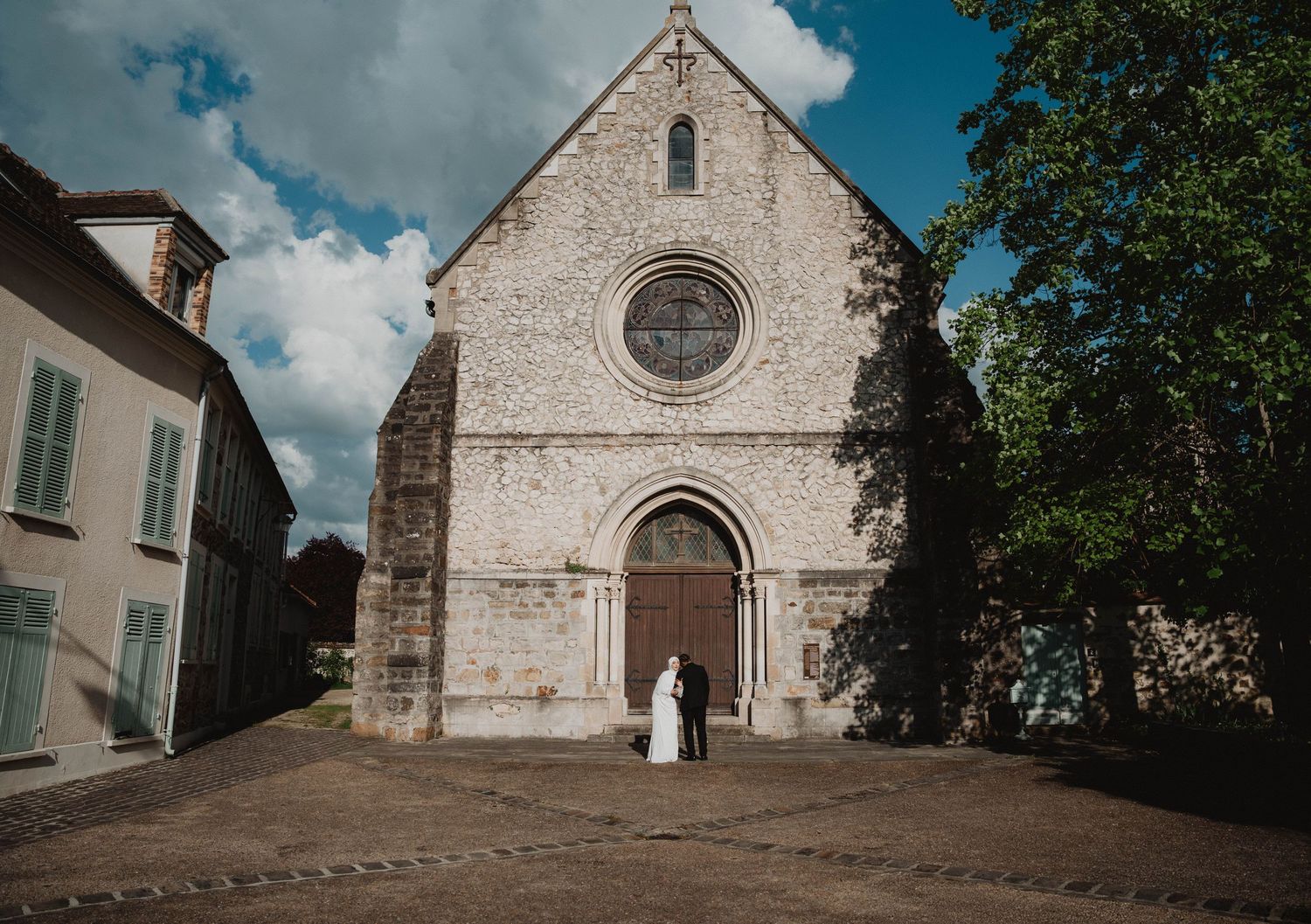 Stone church facade with arched entrance and circular window under cloudy sky.