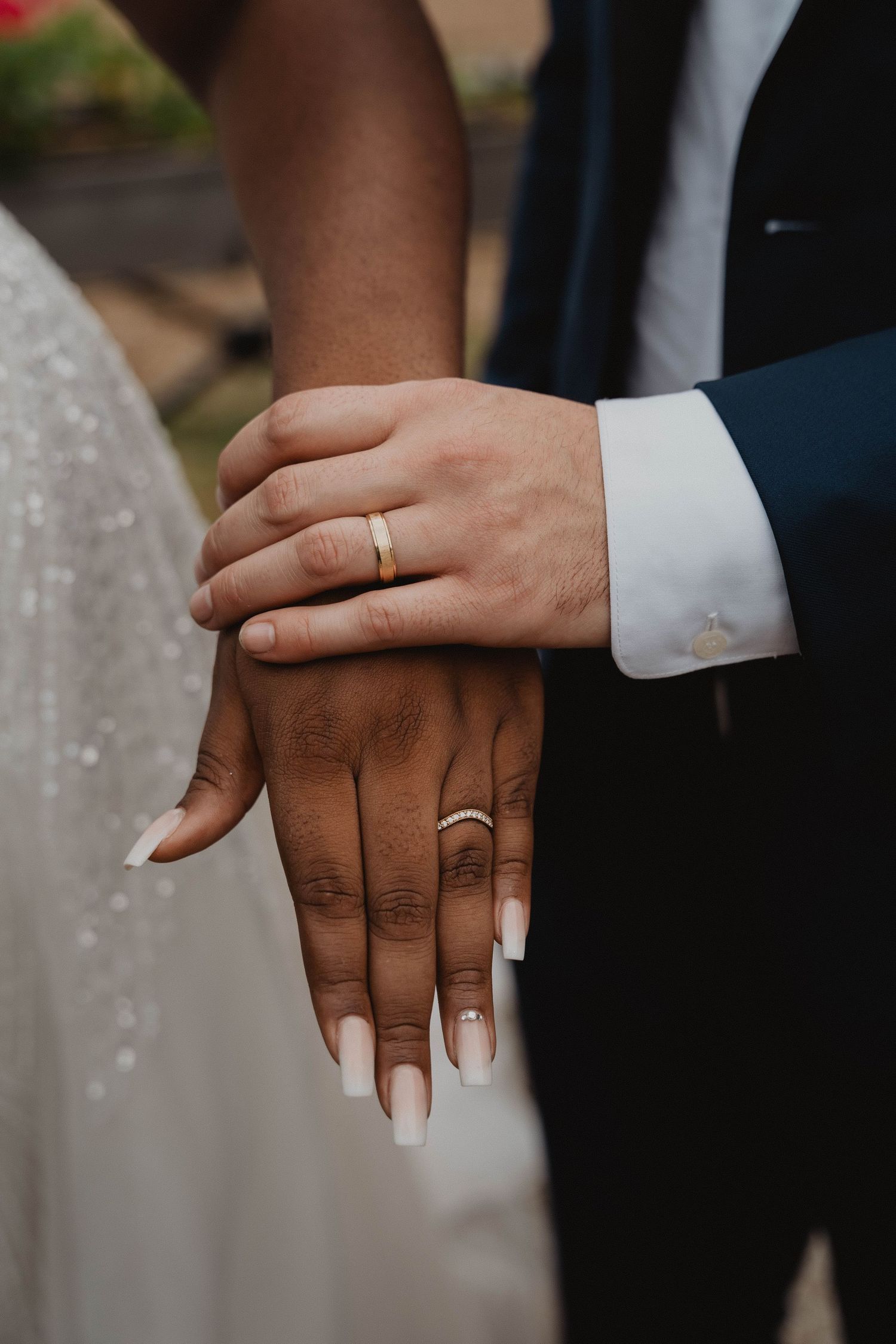 Close-up of intertwined hands showing wedding rings and contrasting skin tones.