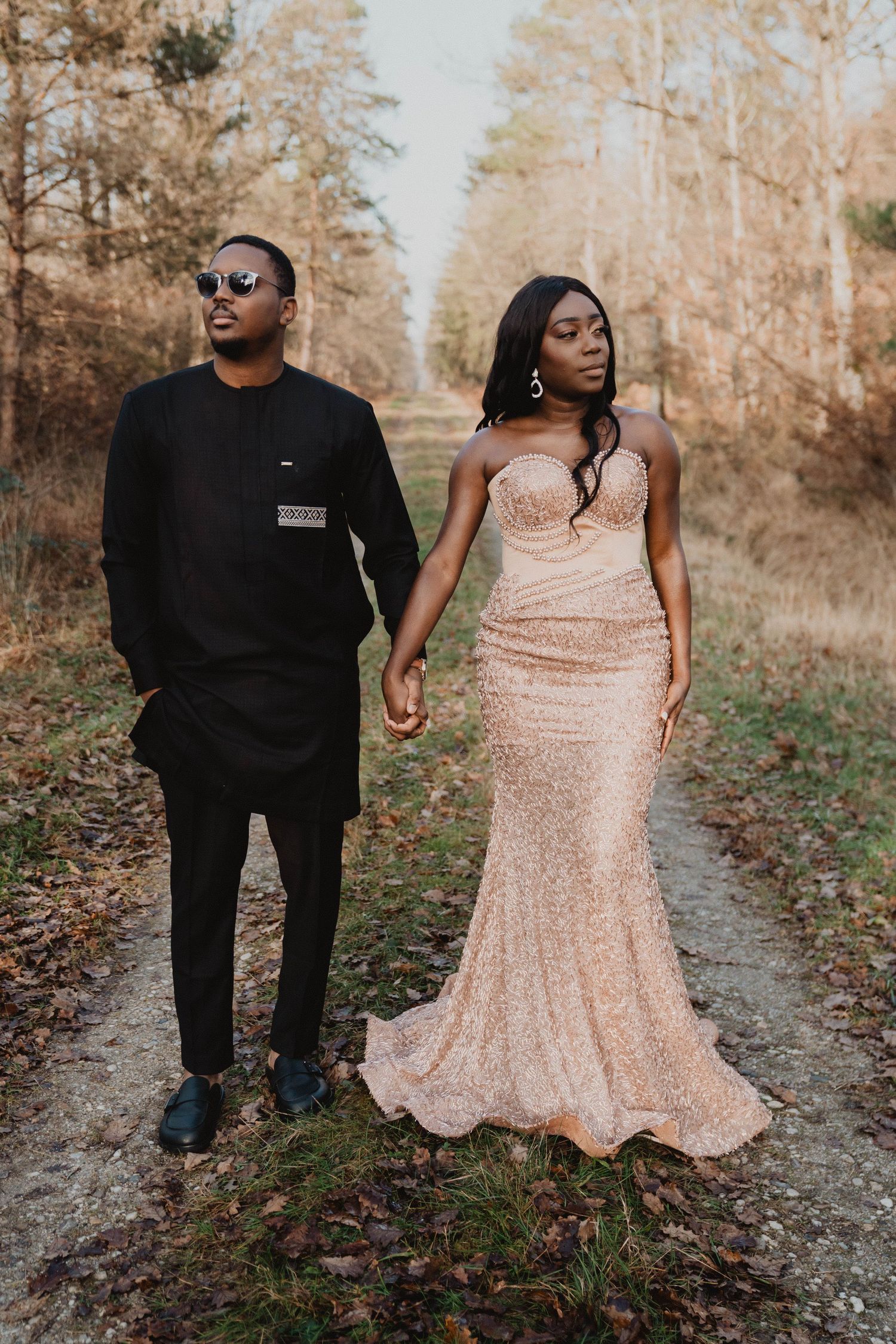 Un couple en tenue de soirée se tient la main en marchant sur un sentier forestier d'automne.