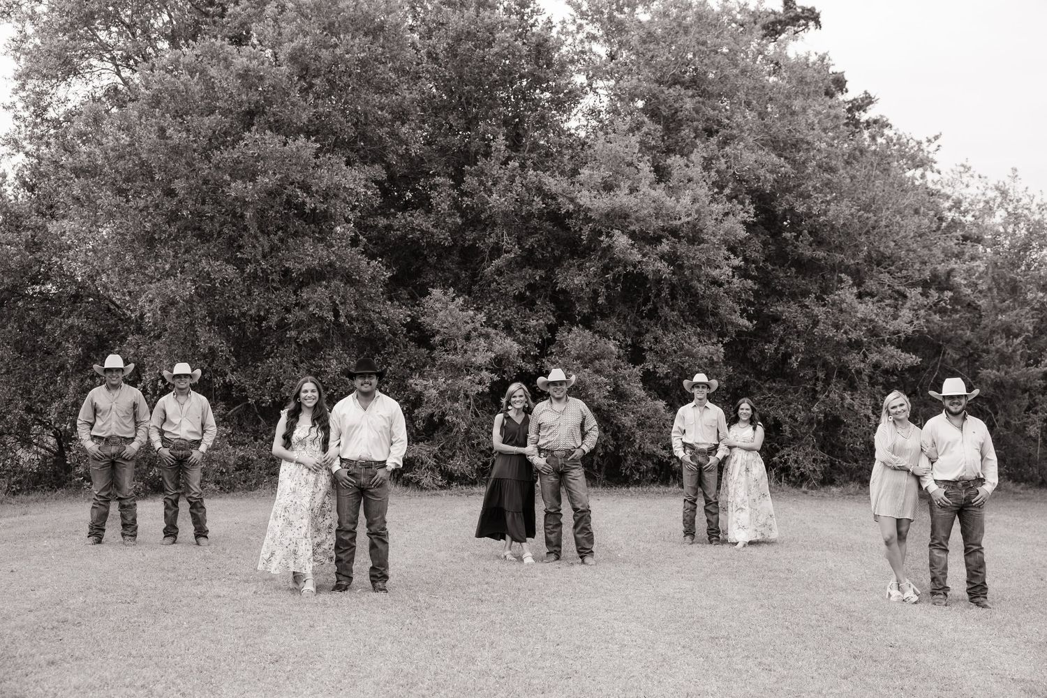 Black and white group photo of nine people in cowboy hats standing in an open field.