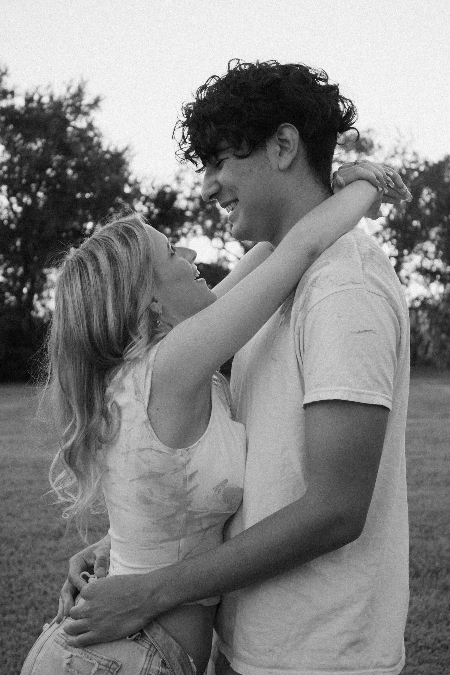 Black and white photo of happy young couple embracing and laughing together in outdoor park.