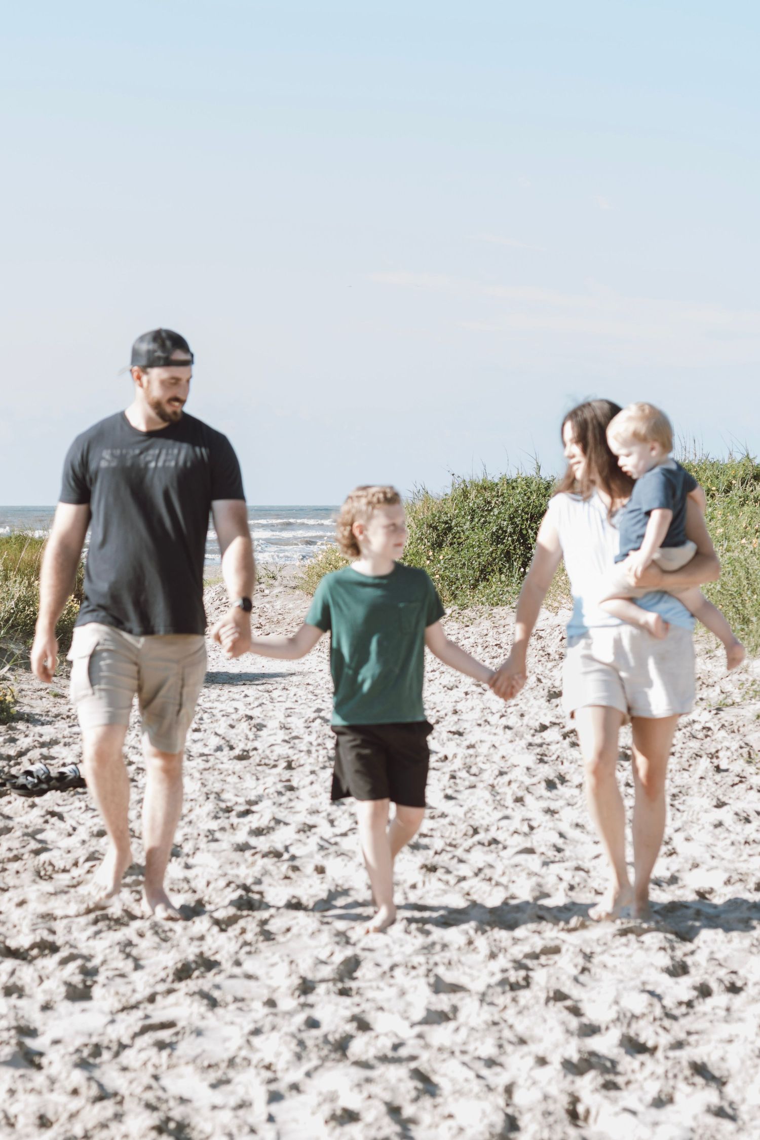 Happy family of four walking barefoot on a sandy beach holding hands on a sunny day.