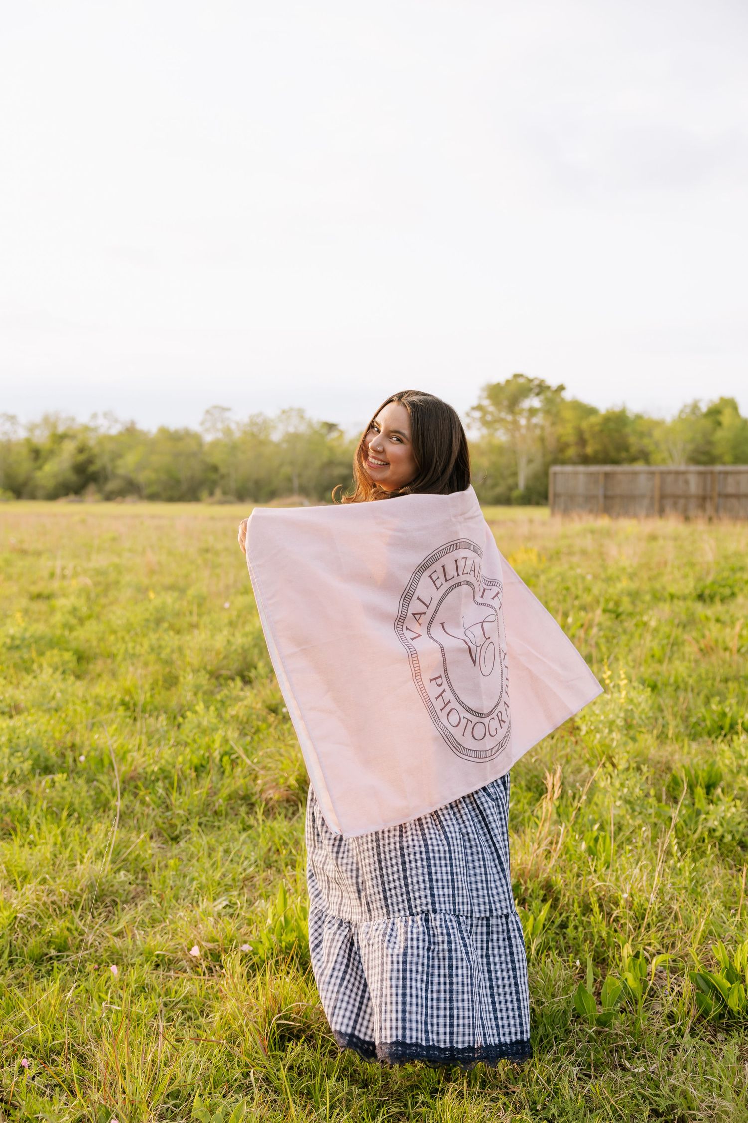 Smiling woman wrapped in a pink blanket standing in a green open field.