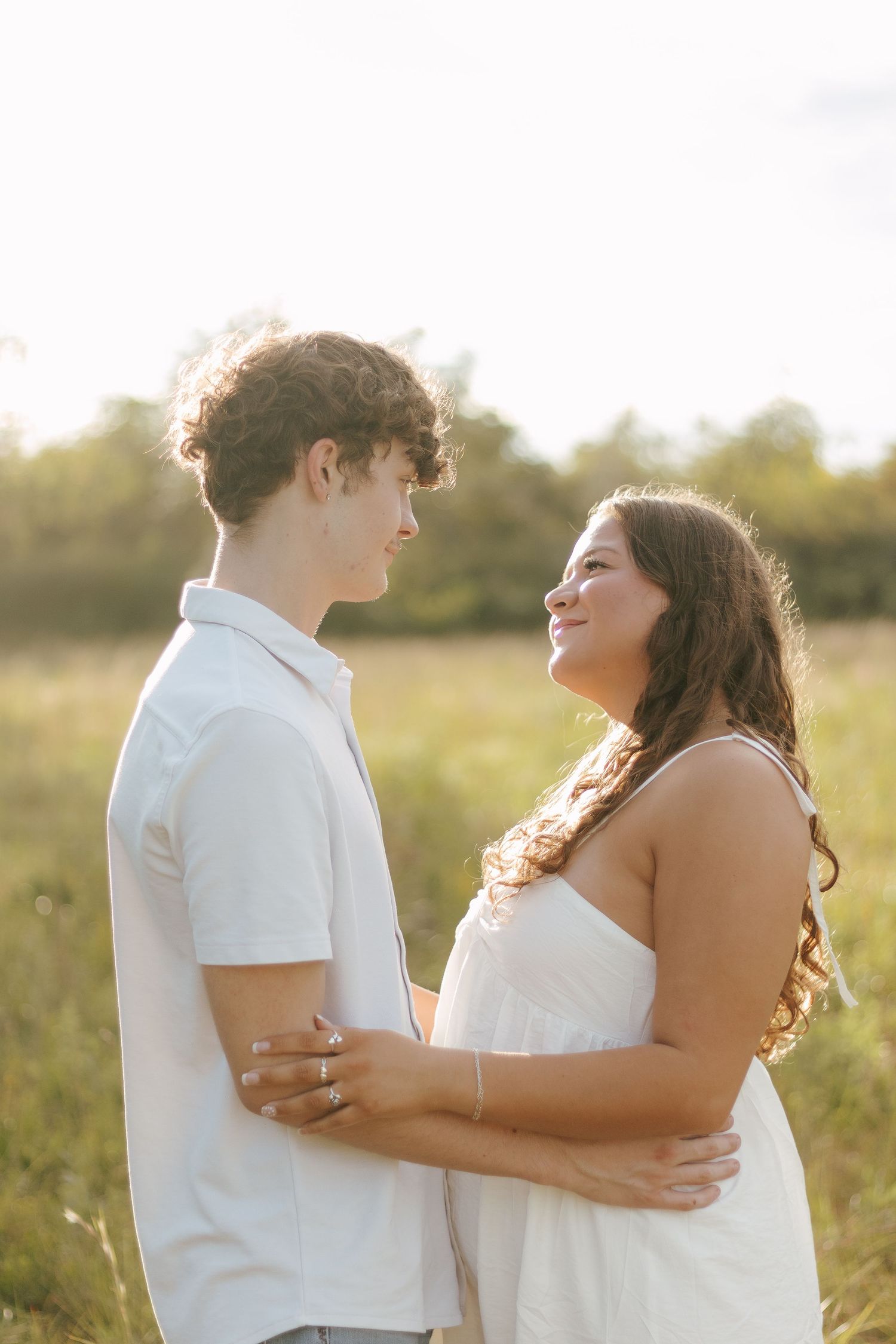 Young couple holding each other and gazing into eyes in sunny golden hour field setting.