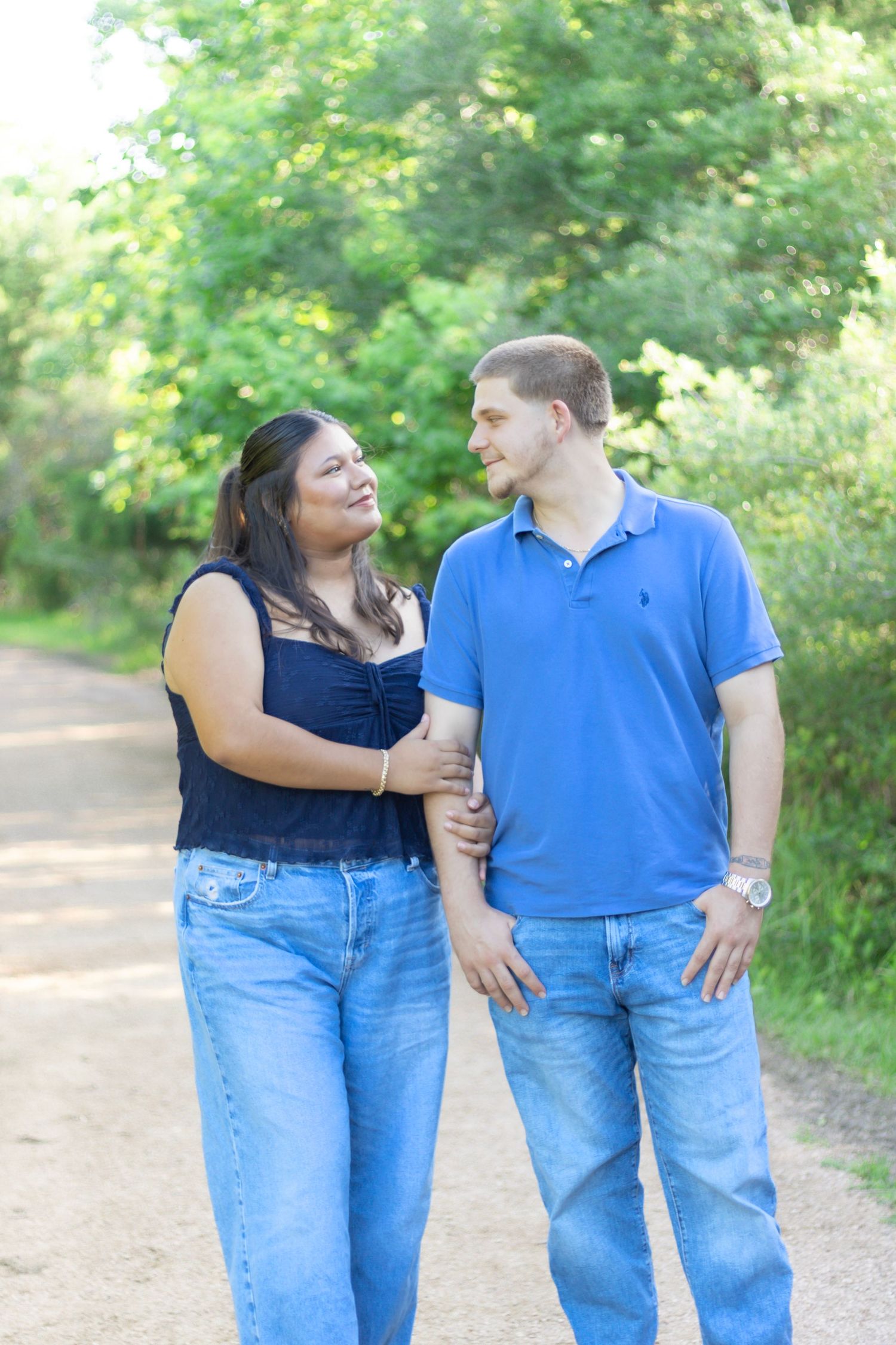Smiling couple walking arm in arm on a tree-lined path, wearing coordinating blue outfits.