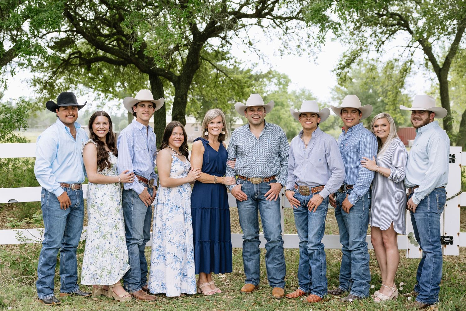 Large family group smiling together outdoors in western attire with cowboy hats.