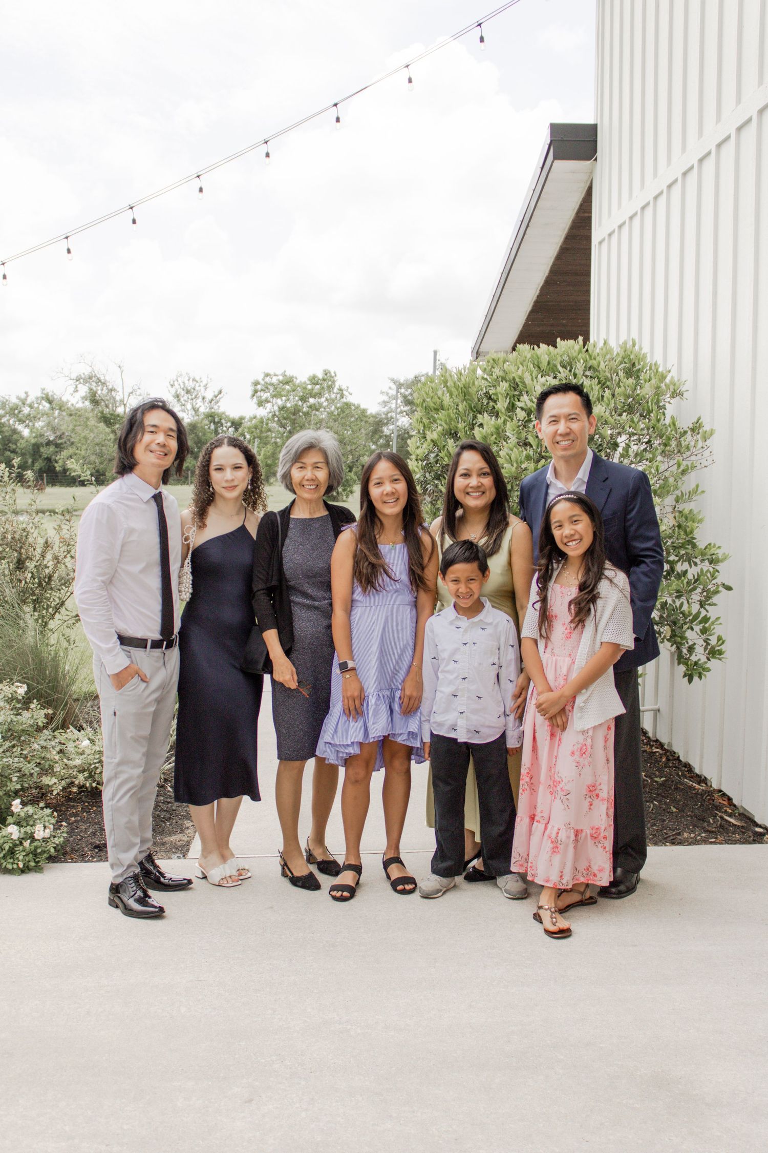 Asian family of eight posing together outdoors at an event venue with string lights in background.