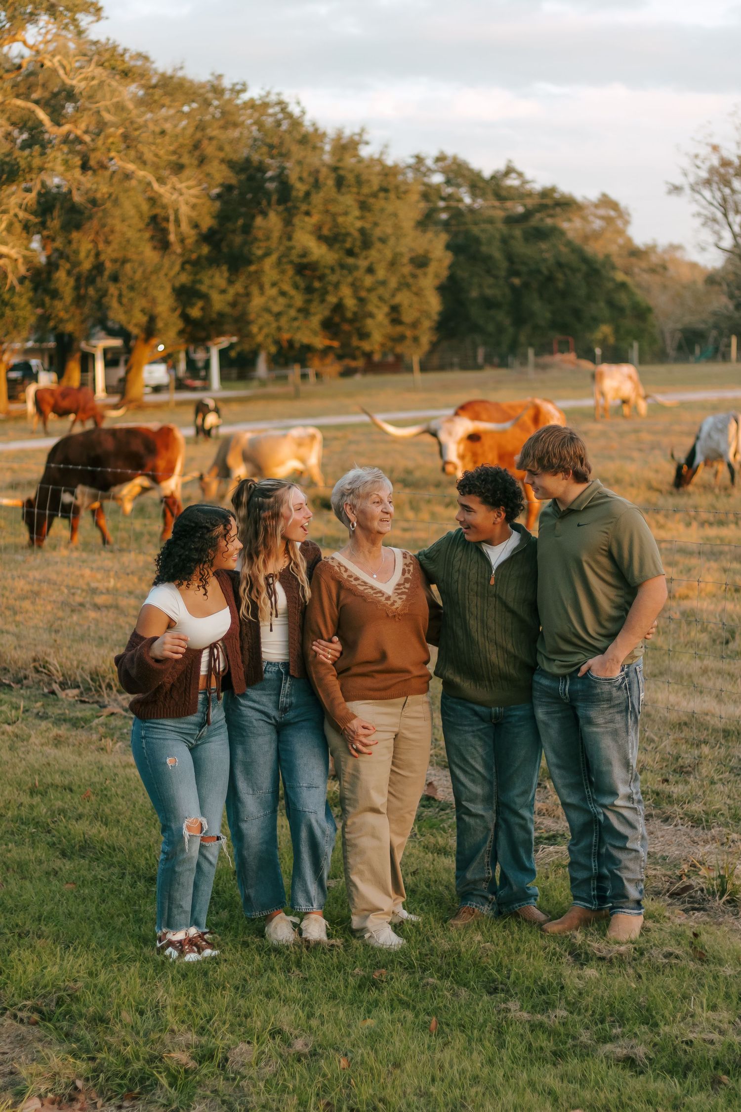 Family of five smiling together in golden hour light with longhorn cattle grazing in background.