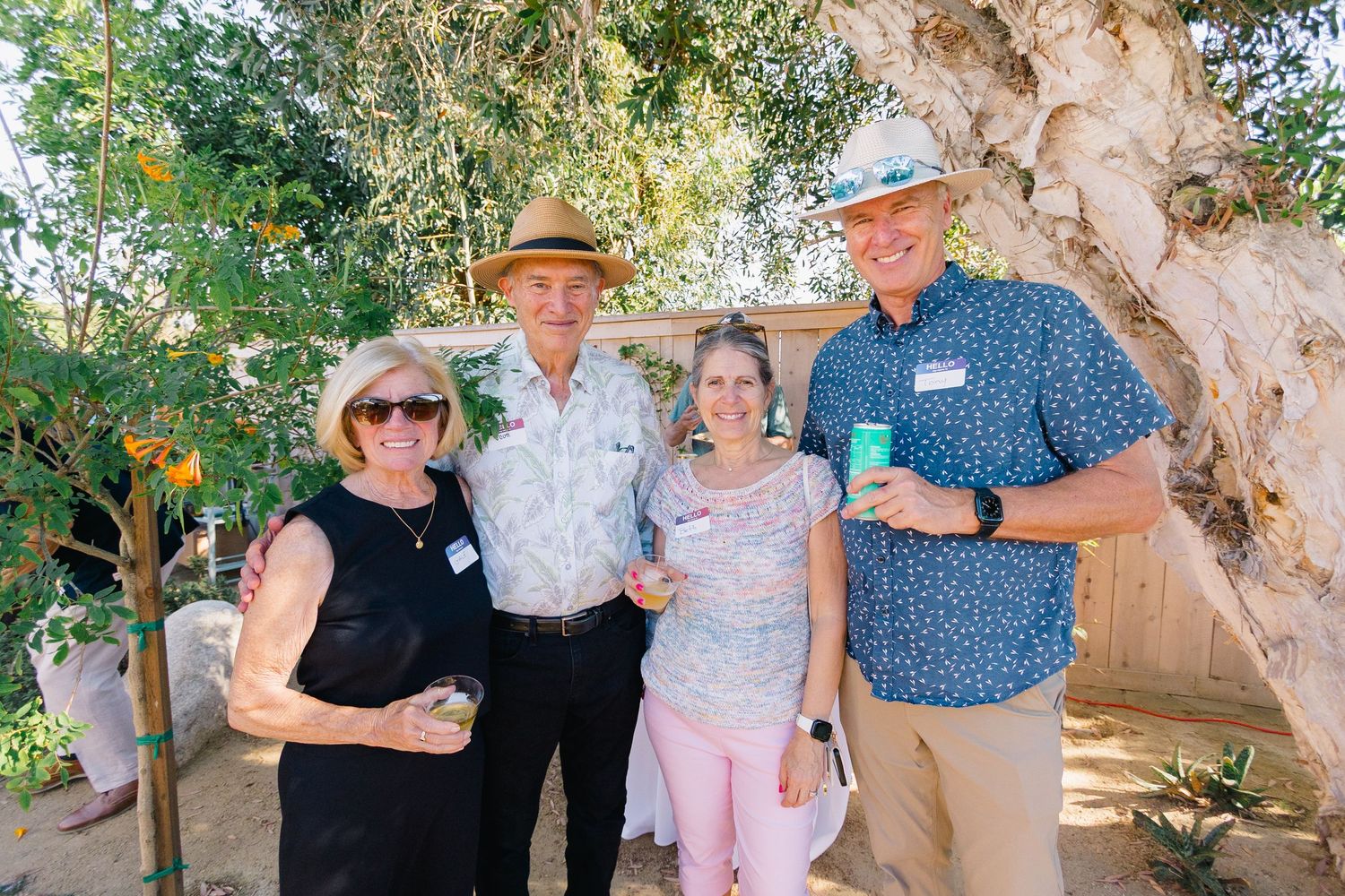 Group of party guests posing together under a large tree at an outdoor event.
