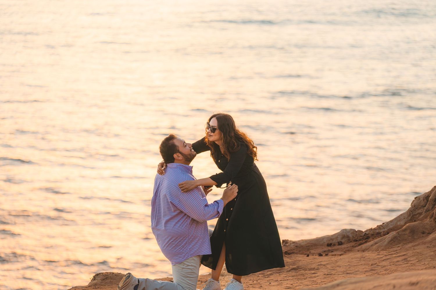 A couple shares a romantic moment on a cliffside overlooking the ocean at dusk.