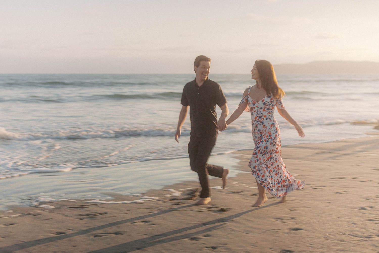 Joyful couple running along the shoreline during golden hour.
