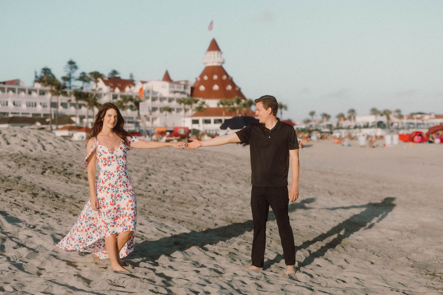 Beachside engagement photos with iconic Hotel del Coronado red turrets in background.