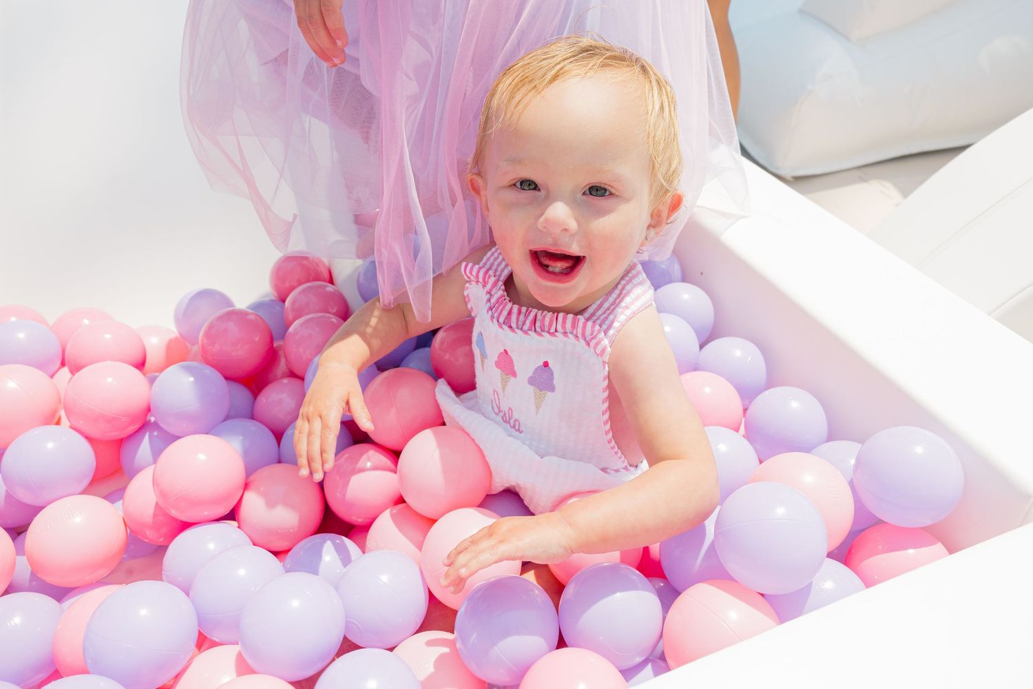 Baby plays in colorful ball pit filled with pink and purple plastic balls.