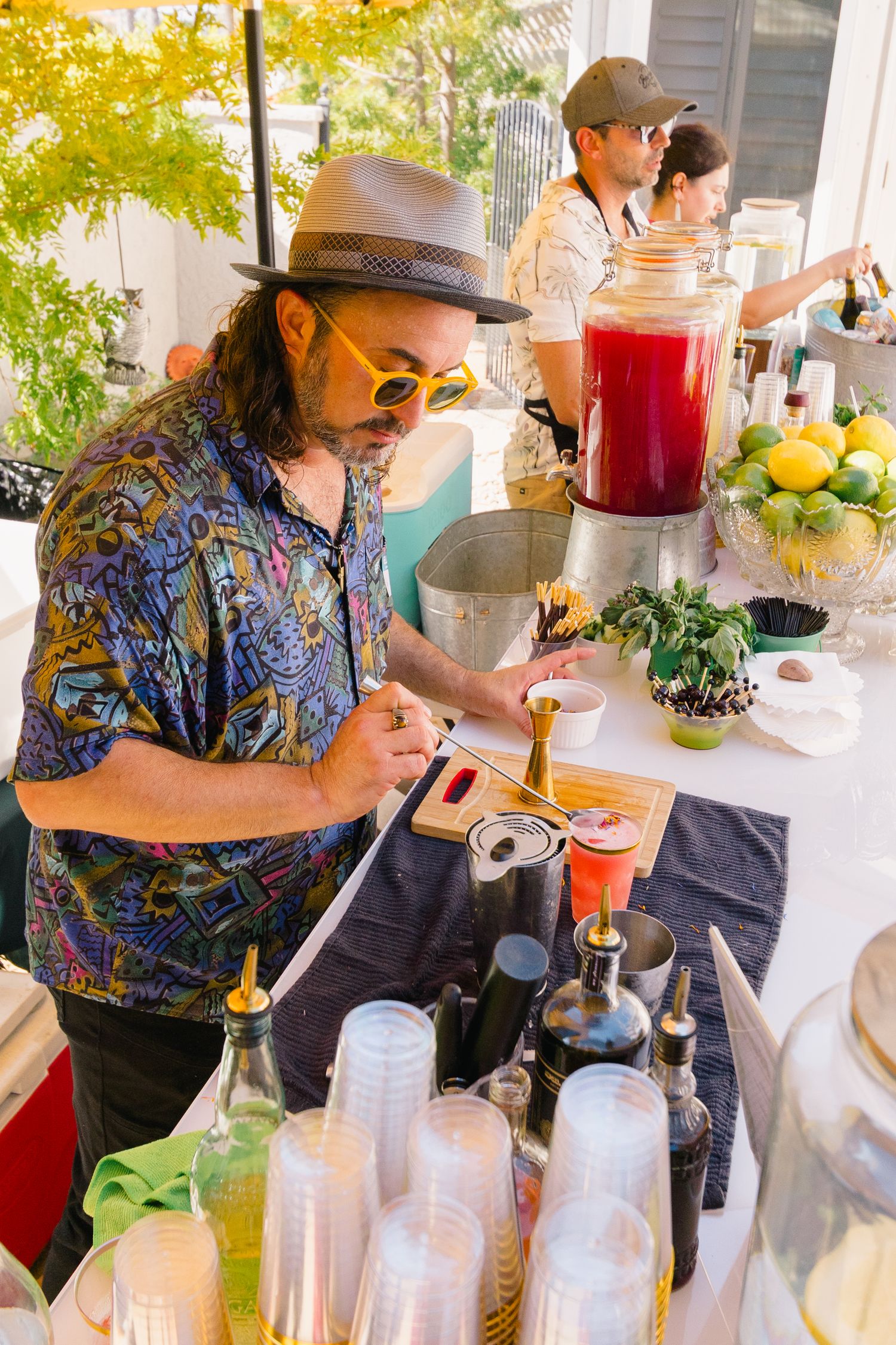 Beverage station with glass dispensers and colorful drinks being served at an outdoor party.