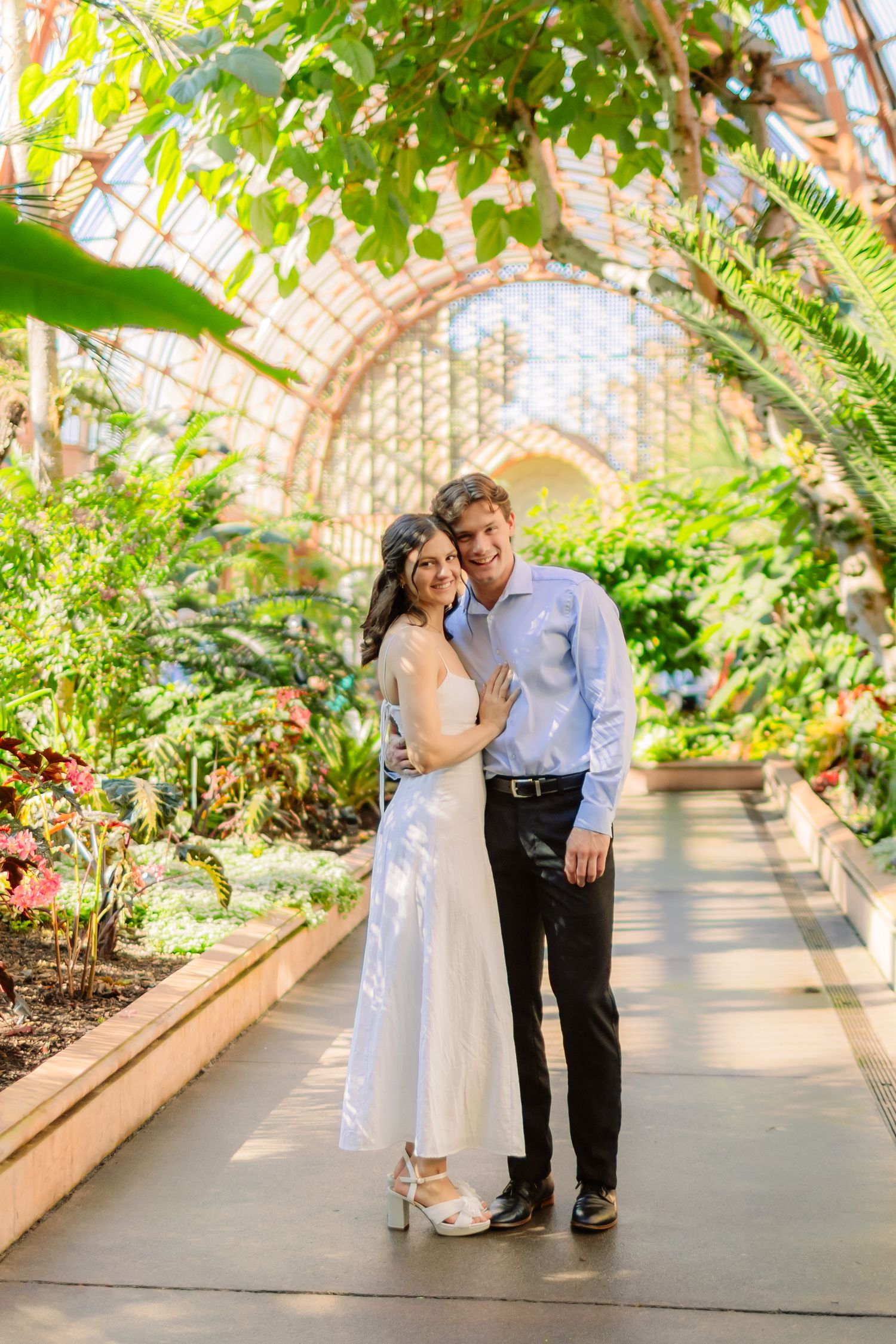A couple poses together in a lush botanical garden conservatory with arched glass ceilings.