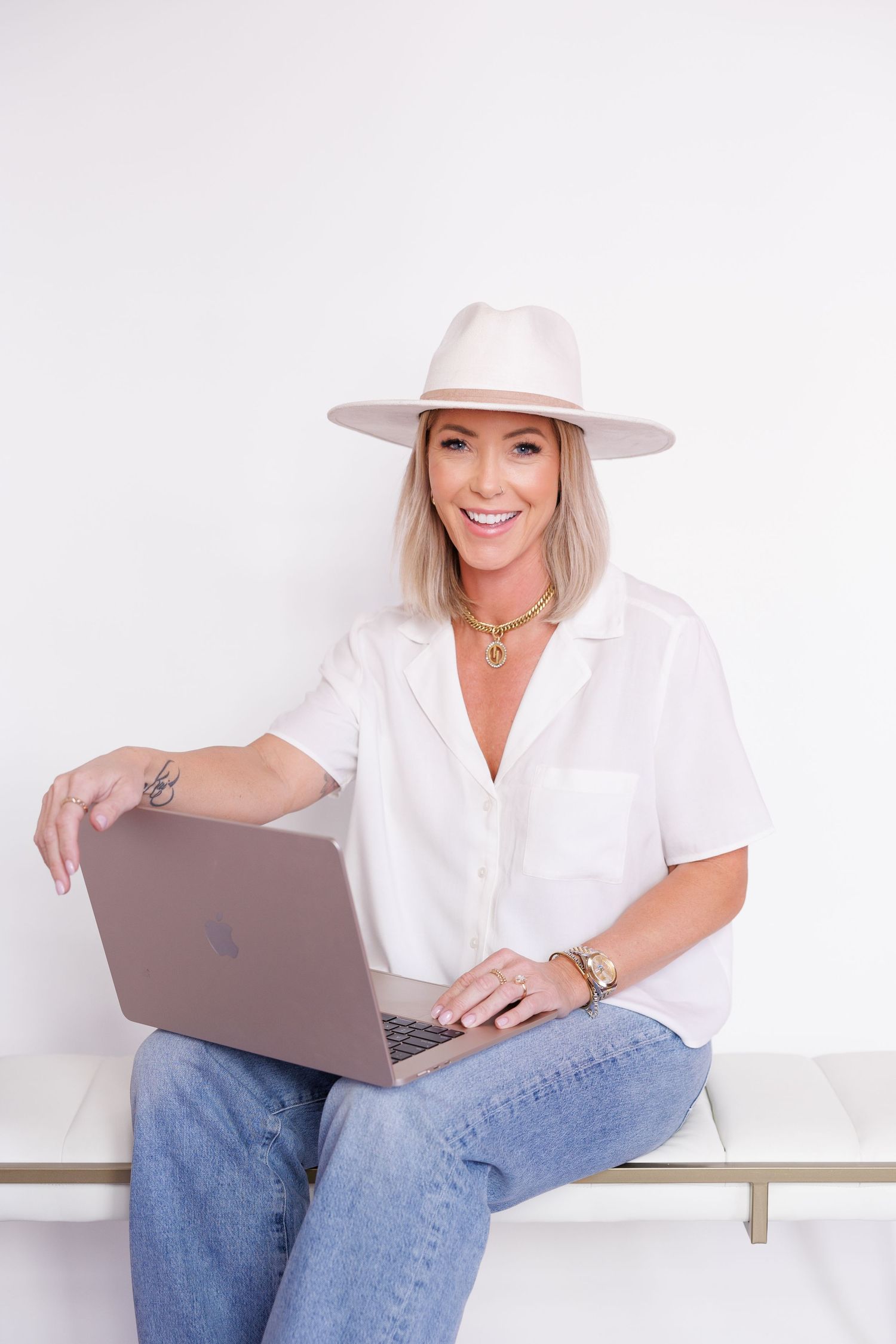 Person wearing white shirt and hat works on laptop while seated indoors.