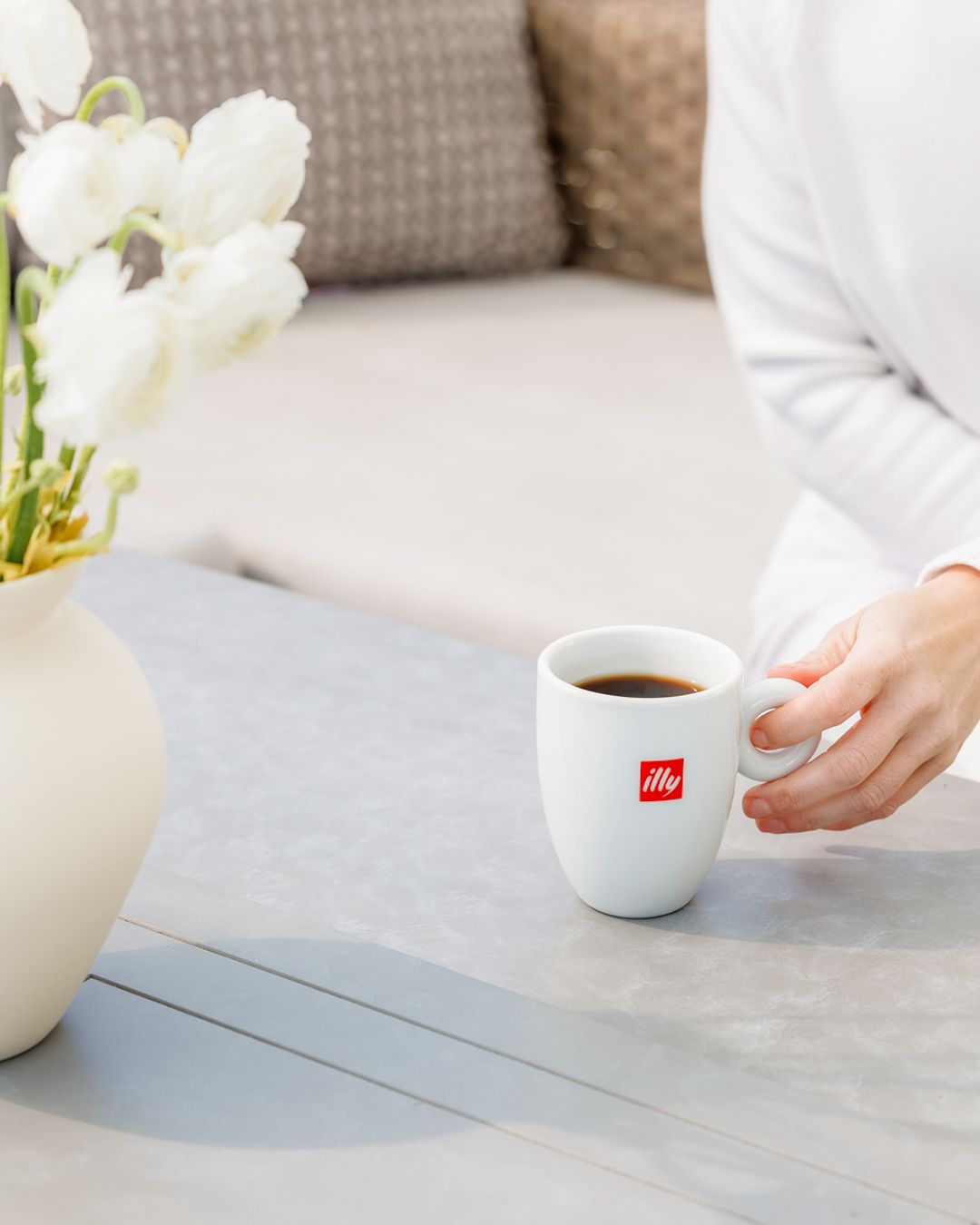 Coffee setting with white illy cup and white tulips on modern grey table.