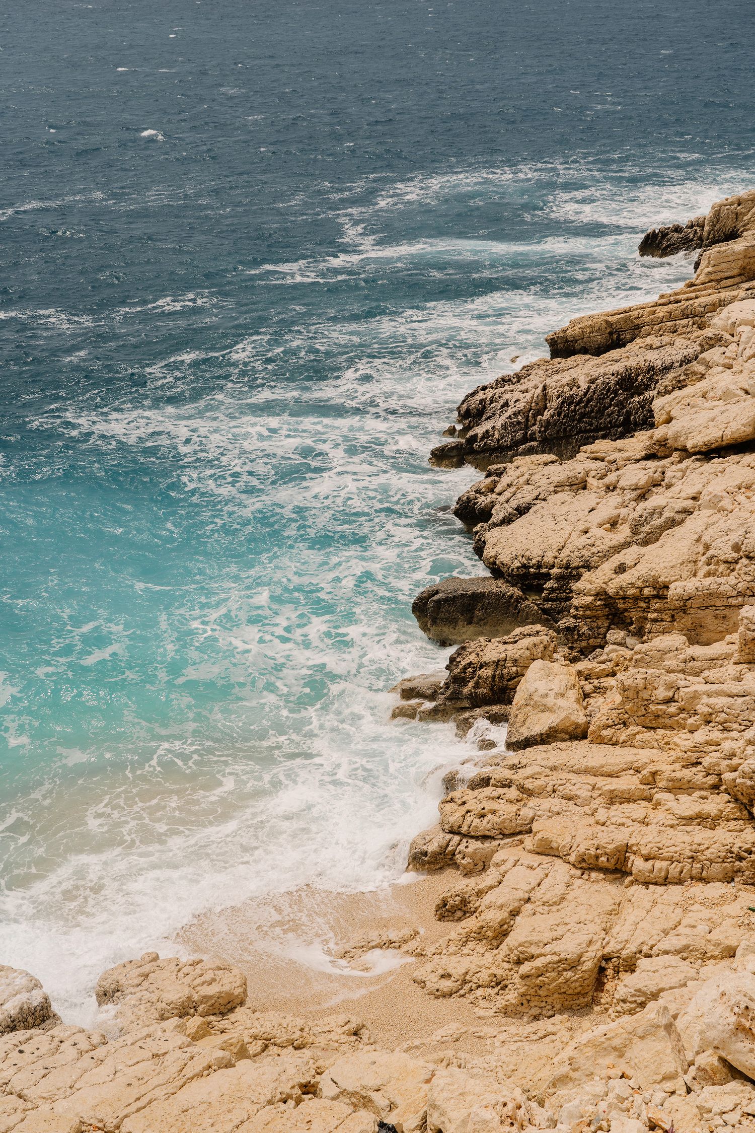 Rugged coastal cliffs meet turquoise ocean waters with white foam waves crashing against the rocky shoreline.