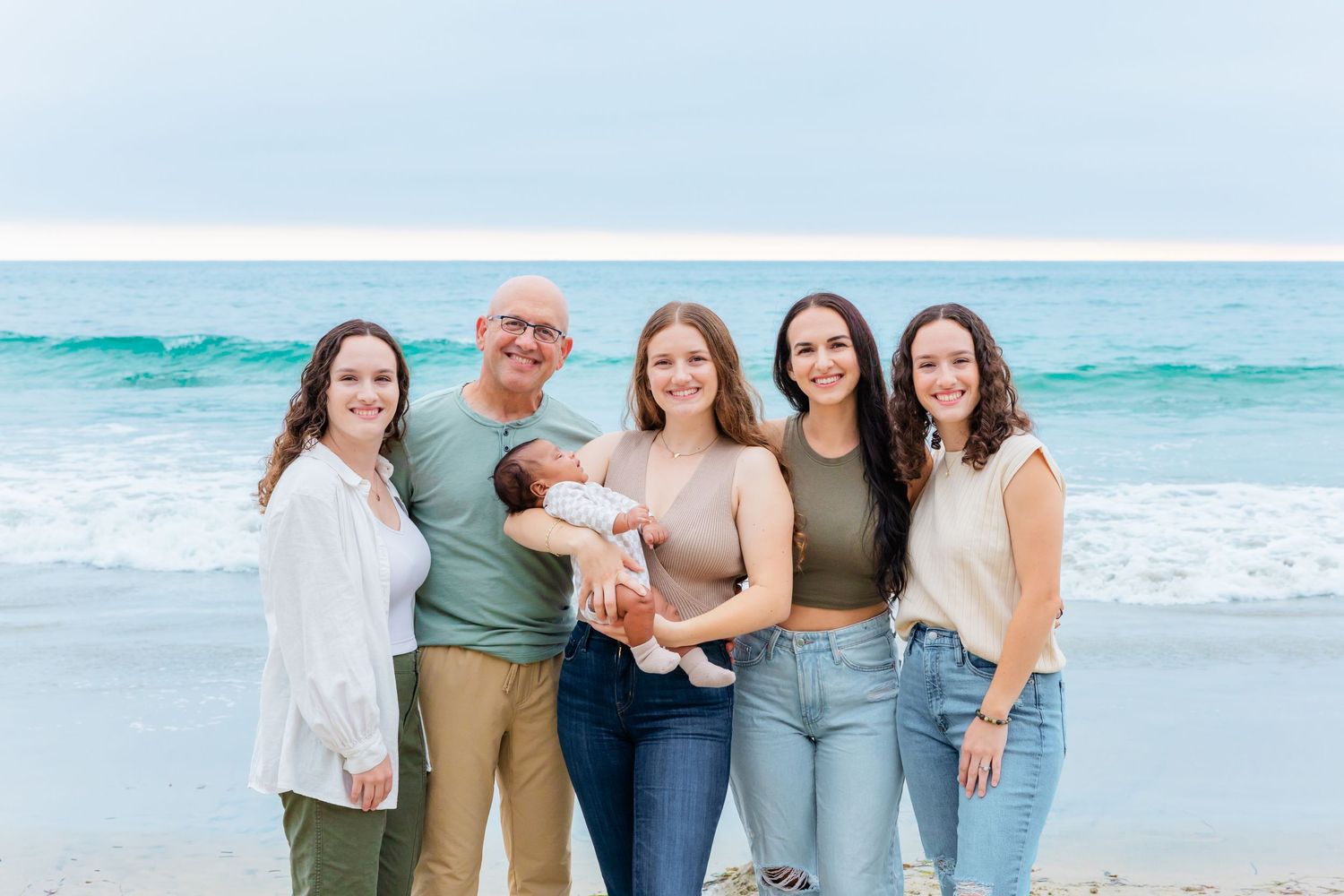 Group photo on a beach with turquoise waves and cloudy sky backdrop.