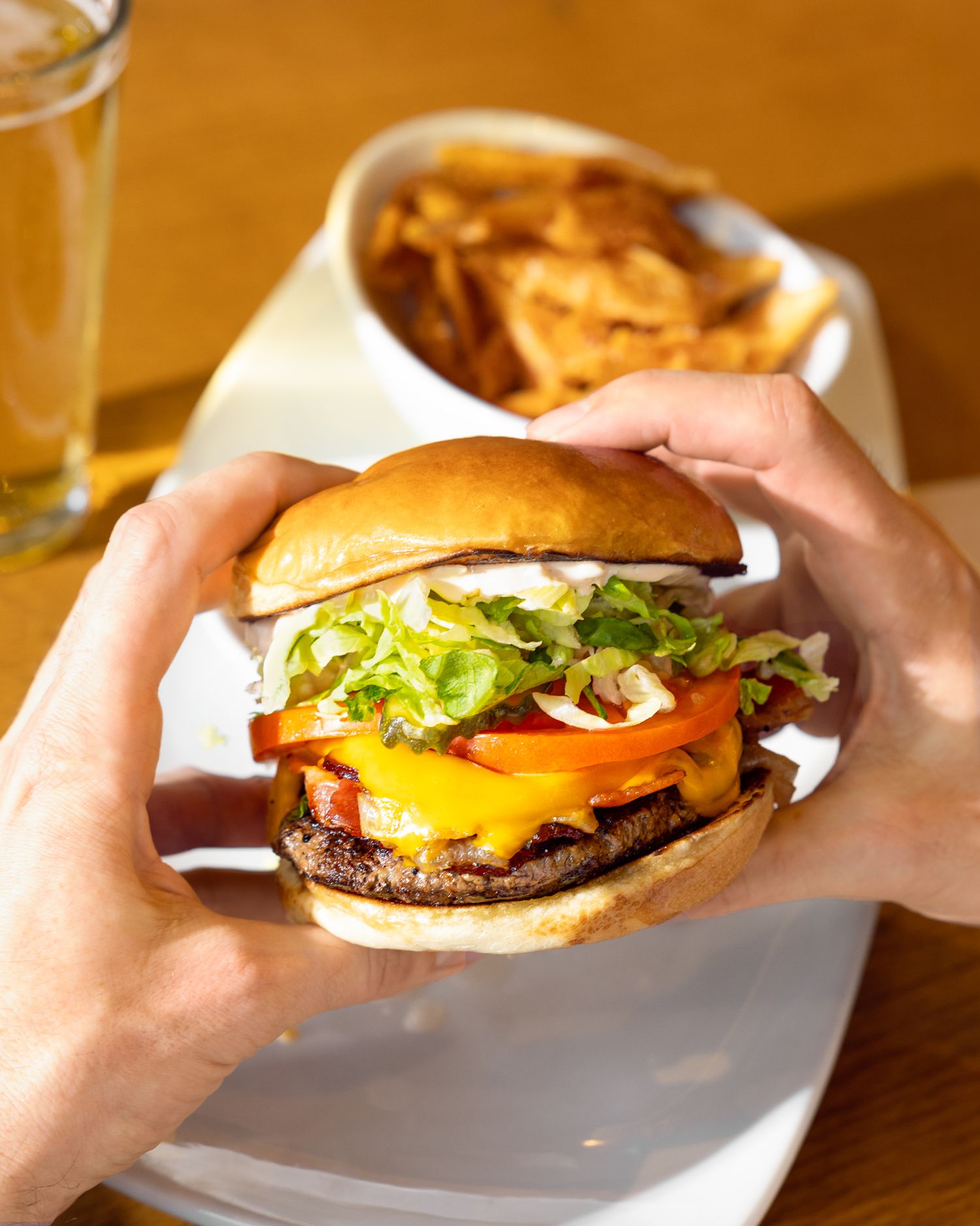 Cheeseburgers with lettuce and tomato being held and served on white plates.