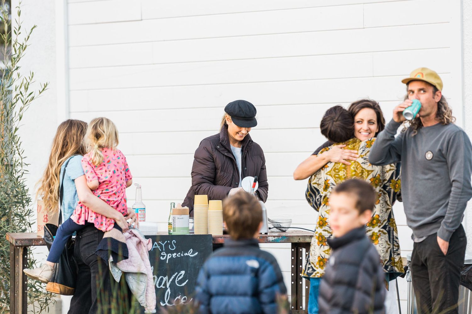 People gather outdoors at a casual event wearing winter coats while socializing and mingling together.