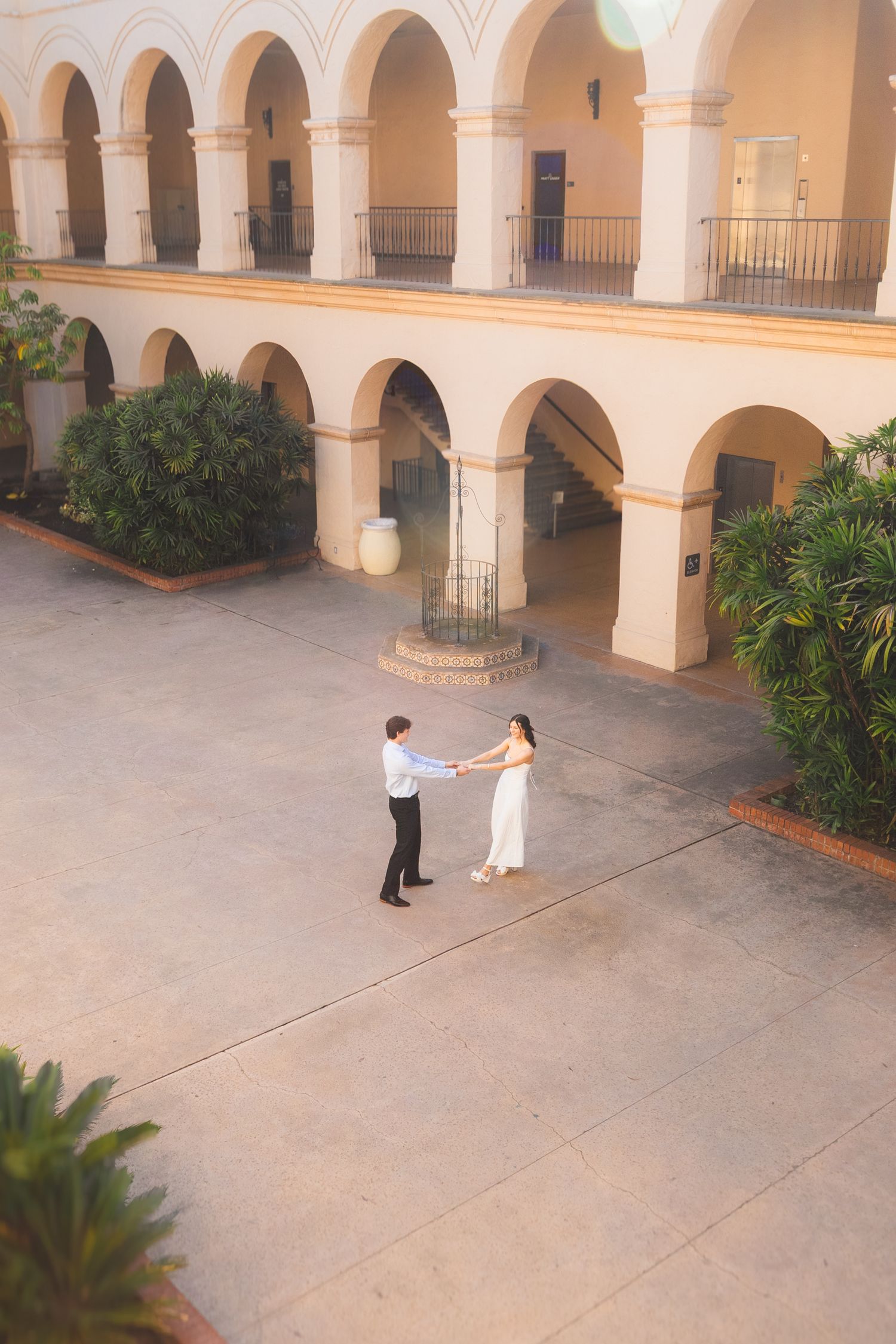 A Spanish colonial courtyard with arched walkways and columns where two people stand in the distance.