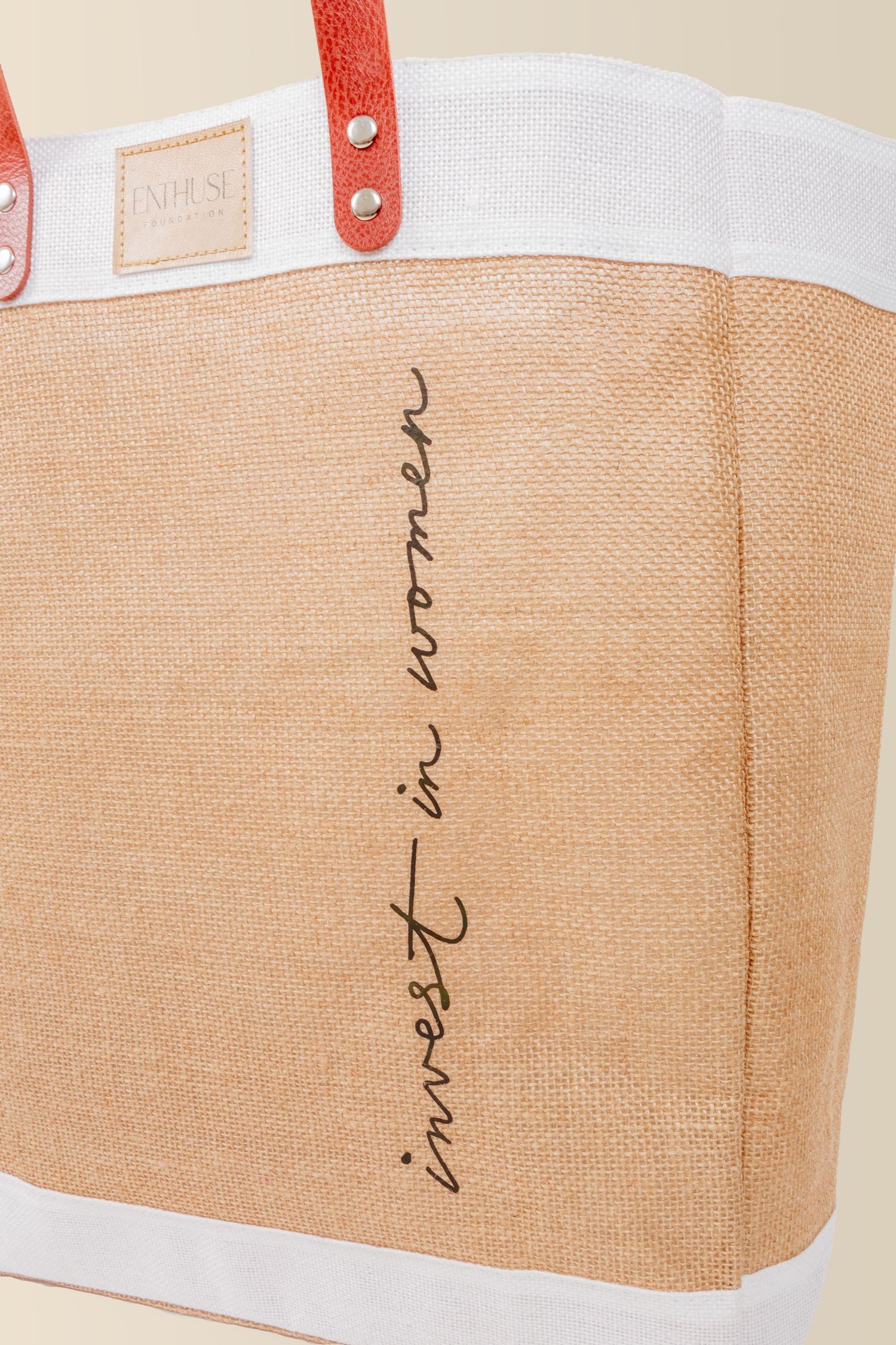 Tan canvas tote bag with white trim and red leather handles featuring cursive text on the side.