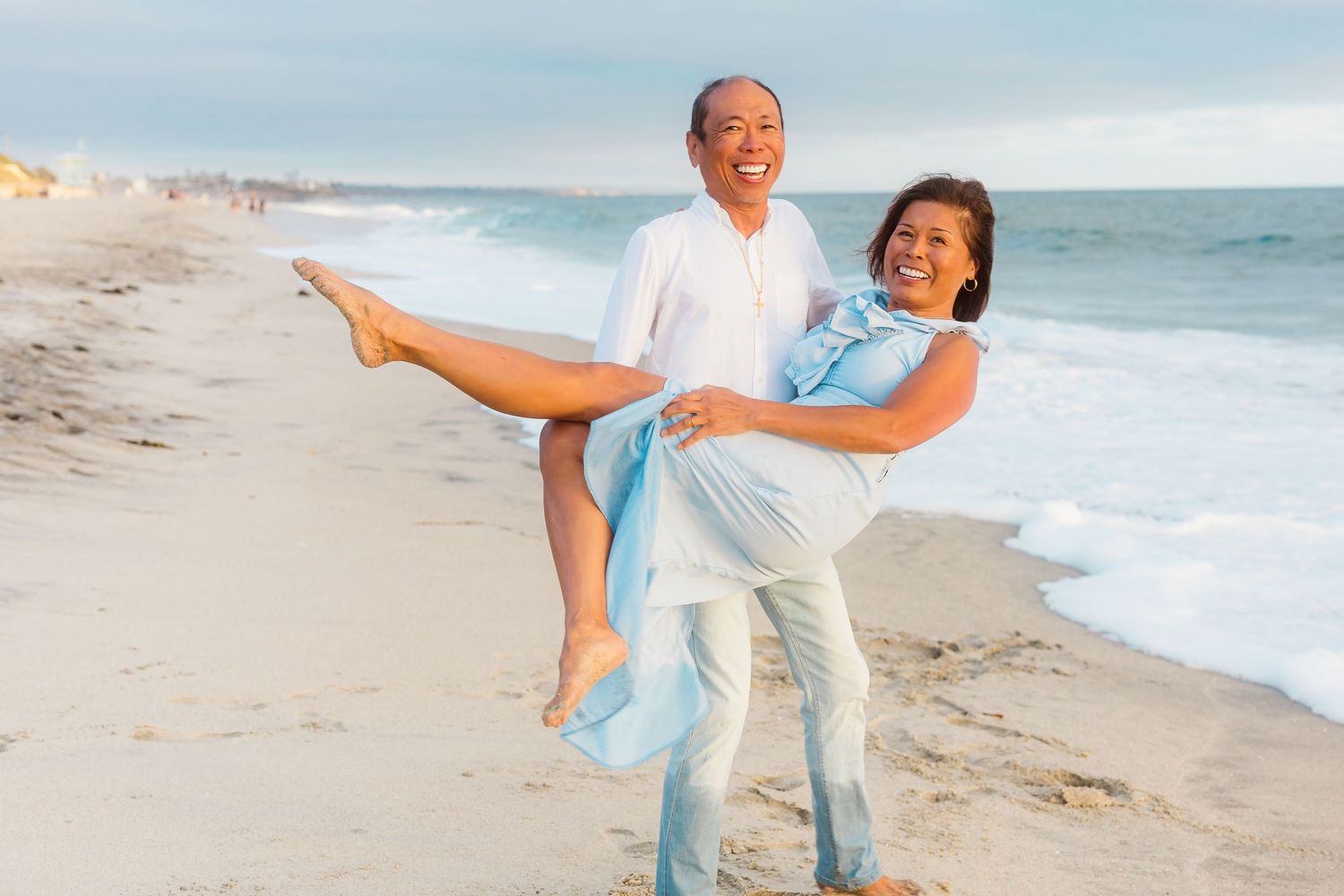 A playful beach portrait of a couple in coordinating blue and white outfits.