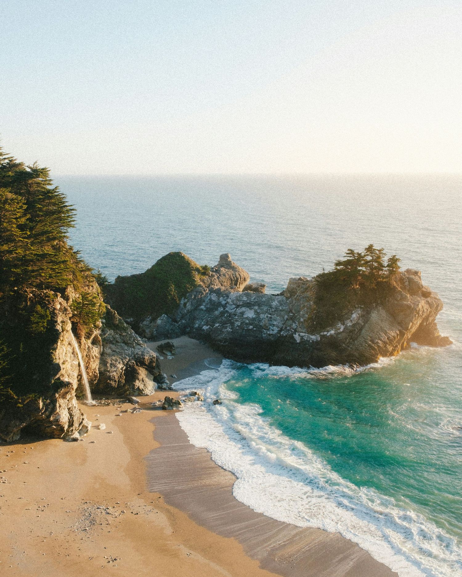 A picturesque beach cove in Big Sur with turquoise waters, rugged cliffs, and a sandy shoreline meeting the Pacific Ocean.