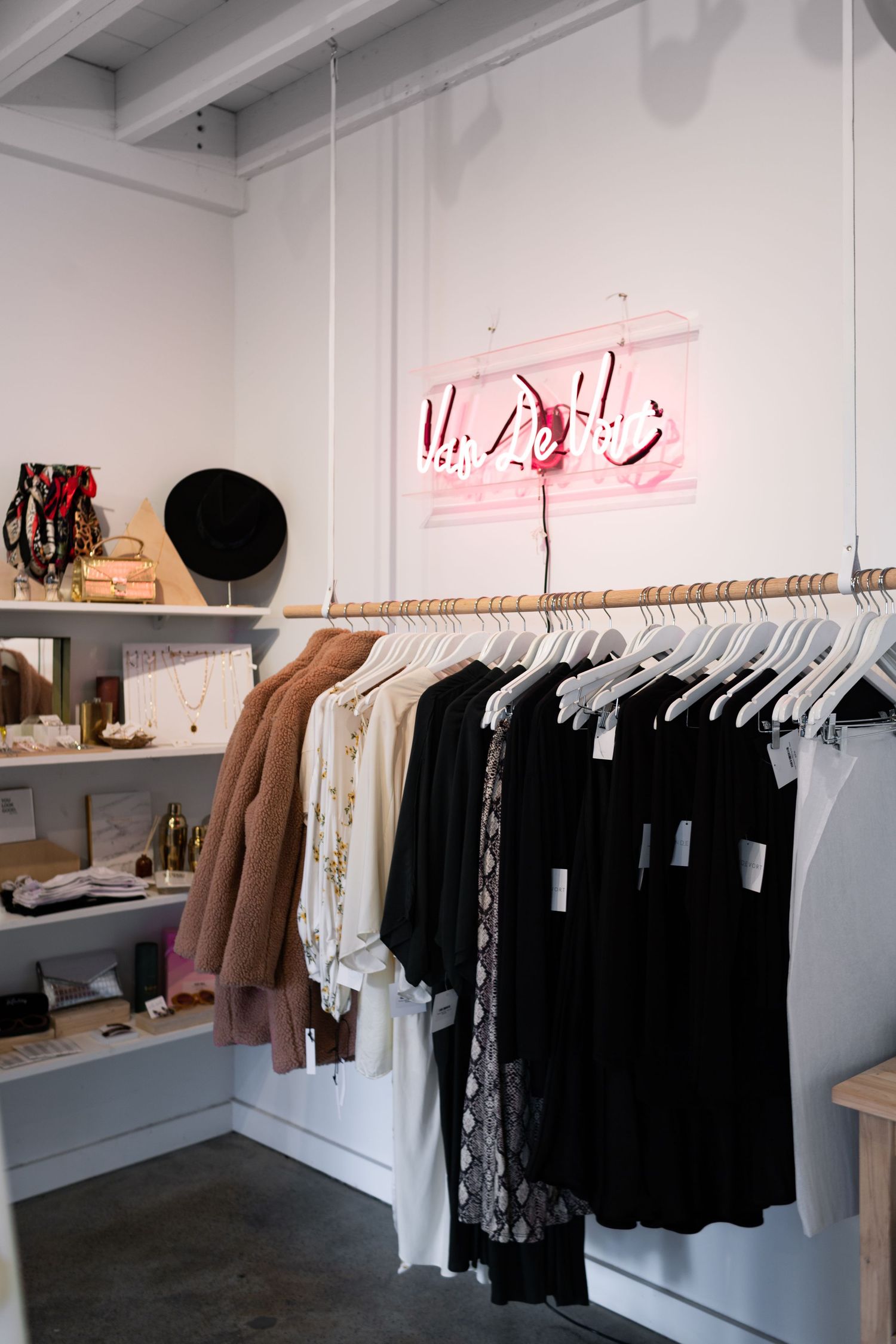 Modern retail clothing store interior with black and white garments hanging neatly on racks beneath pink neon lighting.