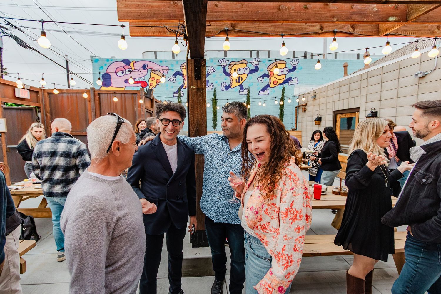 A festive outdoor gathering with string lights and colorful murals decorating the walls.