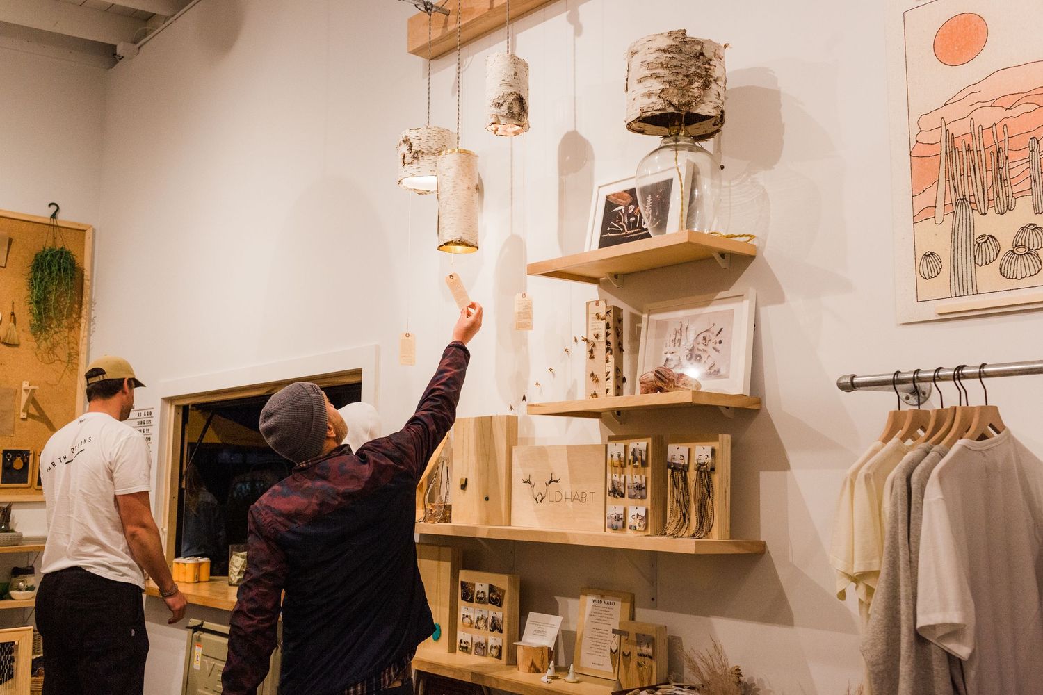 Artists work collaboratively in a bright studio space with artwork displayed on white walls and wooden shelving.