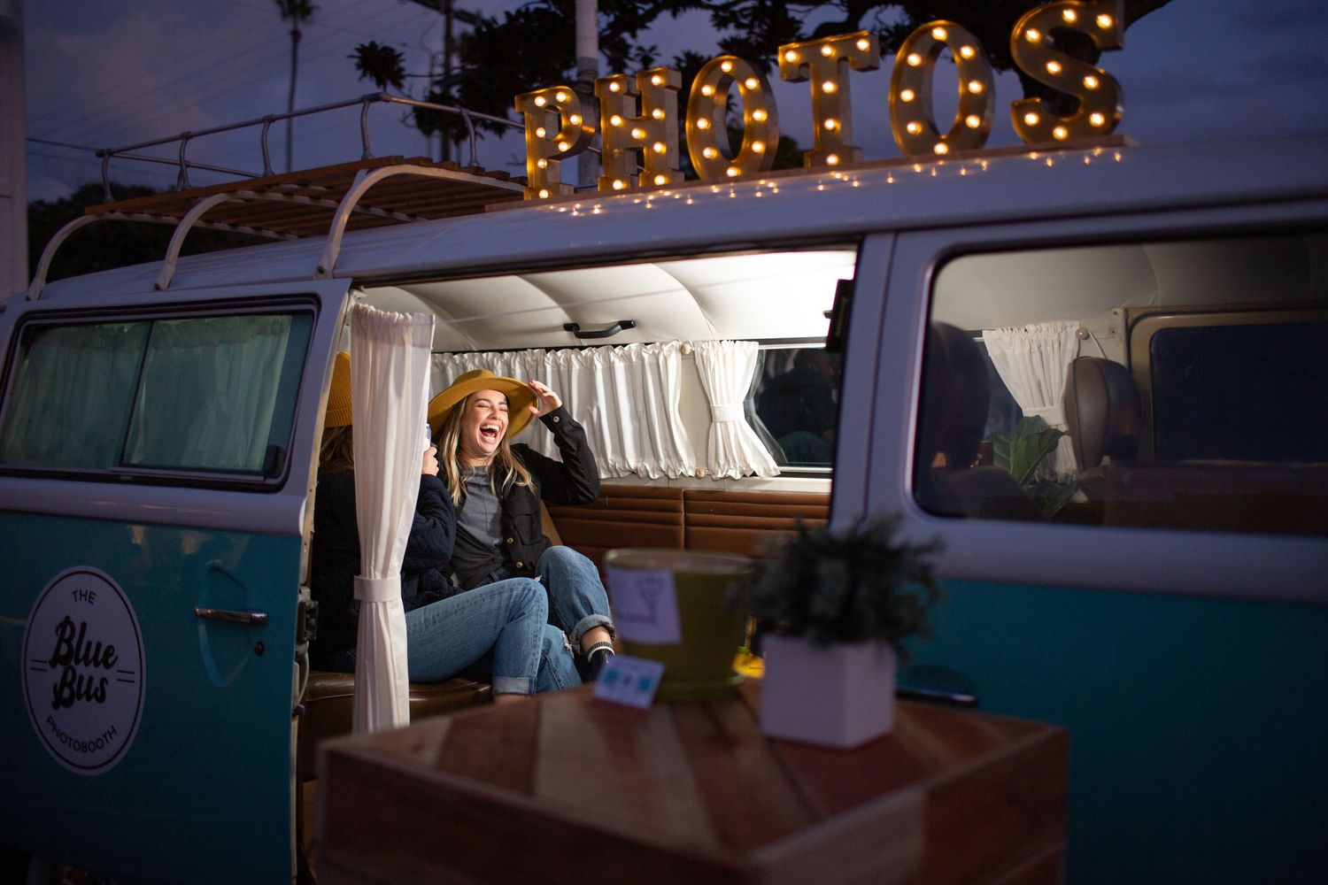Classic retro VW bus lineup at sunset with string lights glowing overhead at a vintage car gathering.