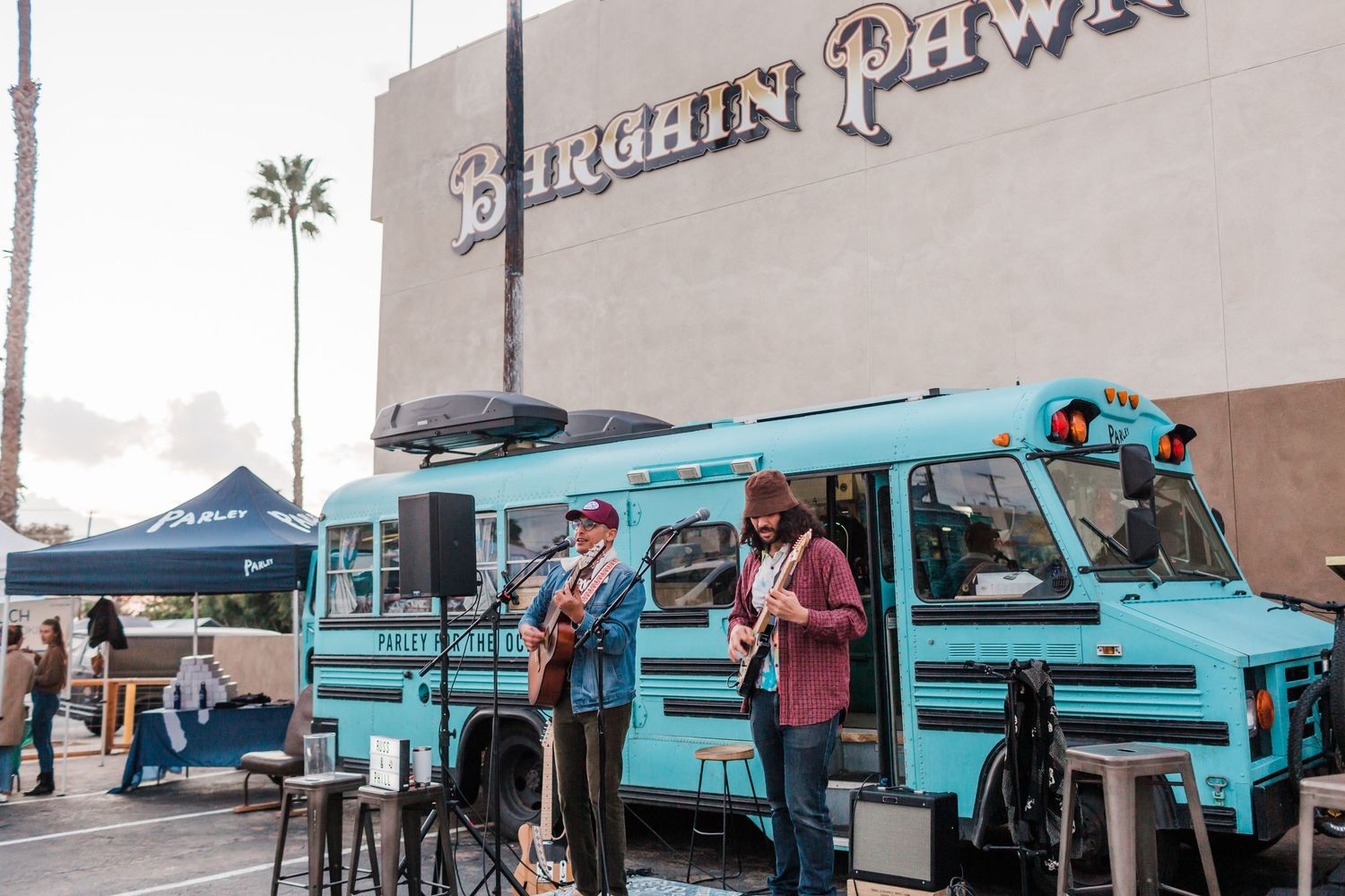 A line of bright turquoise food trucks and vendor tents set up at an outdoor event venue.