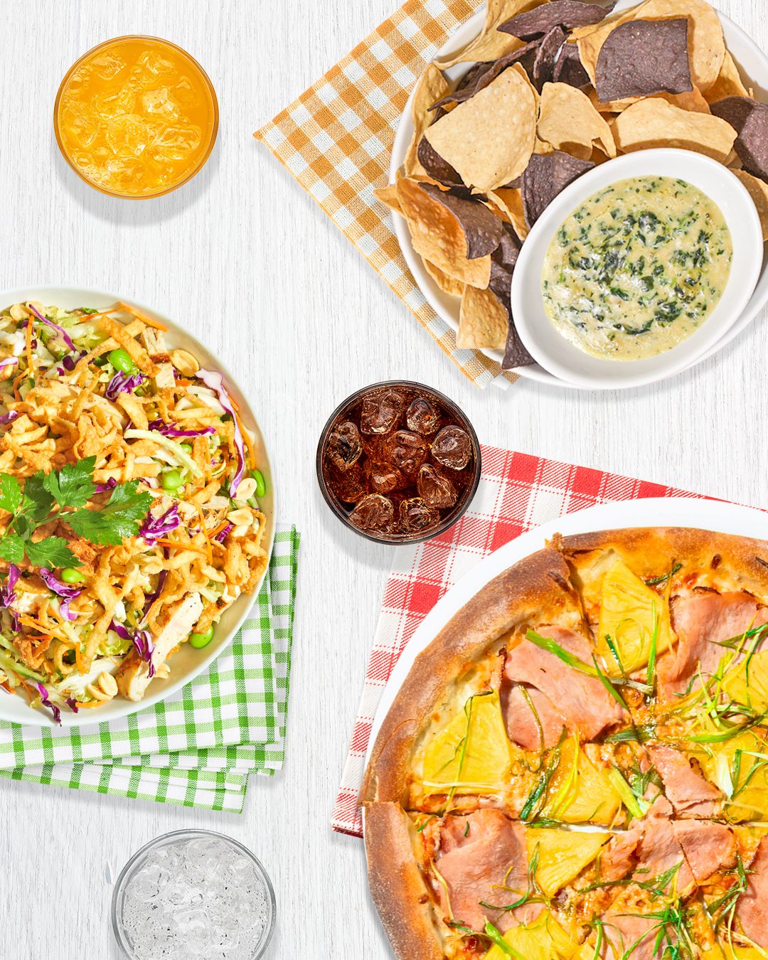 Party spread featuring pizzas, dipping sauces and coleslaw on checkered napkins.