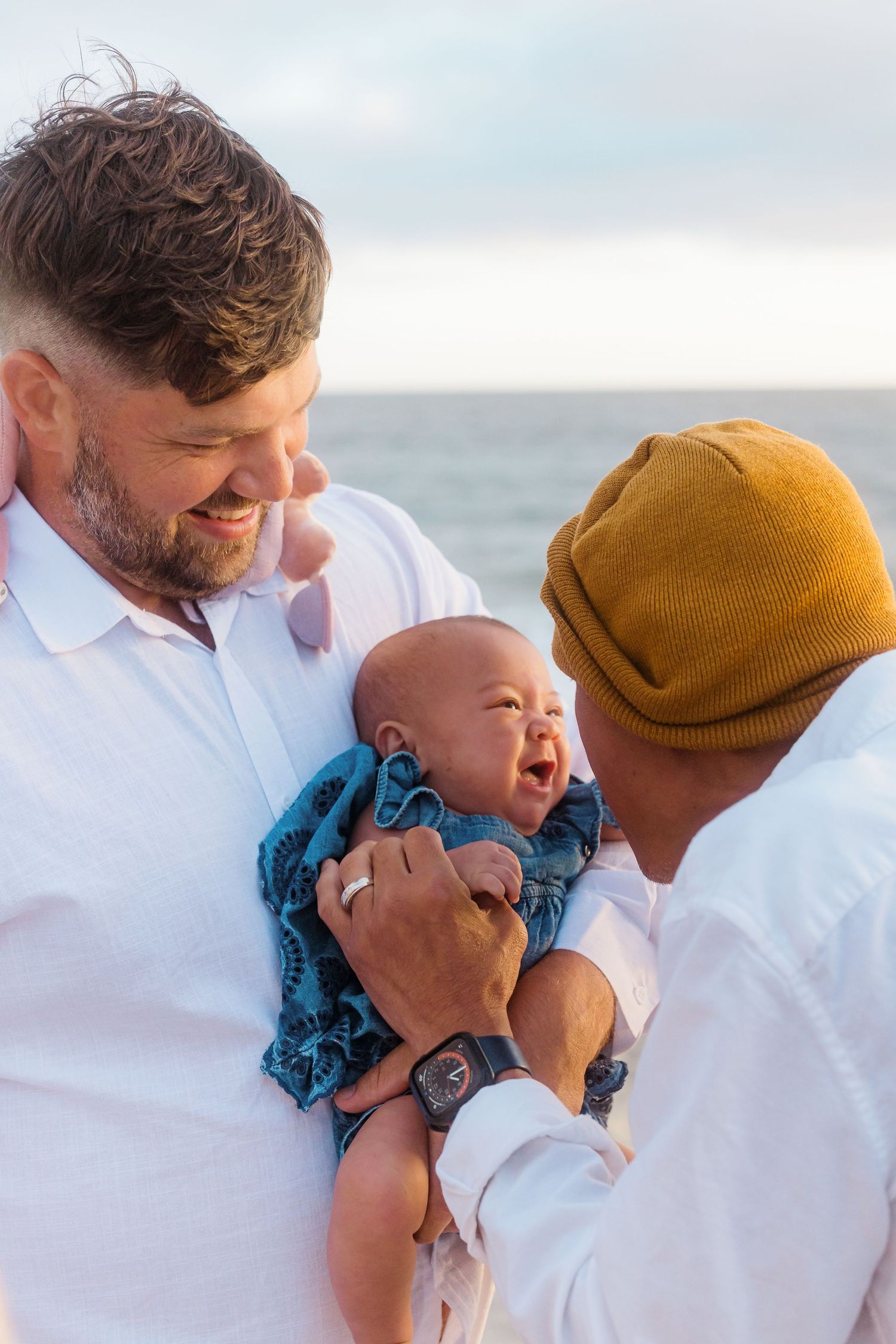 A baby laughing with joy while being held at the beach.