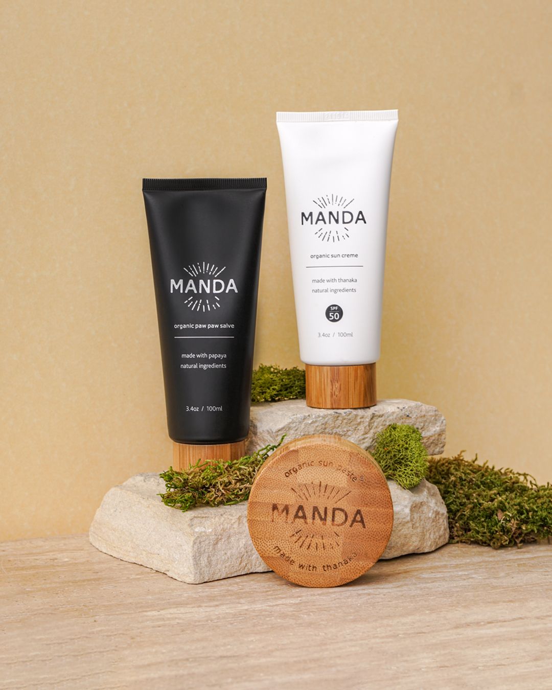 Manda brand cosmetic products with black and white packaging displayed on stone surfaces with moss accents.