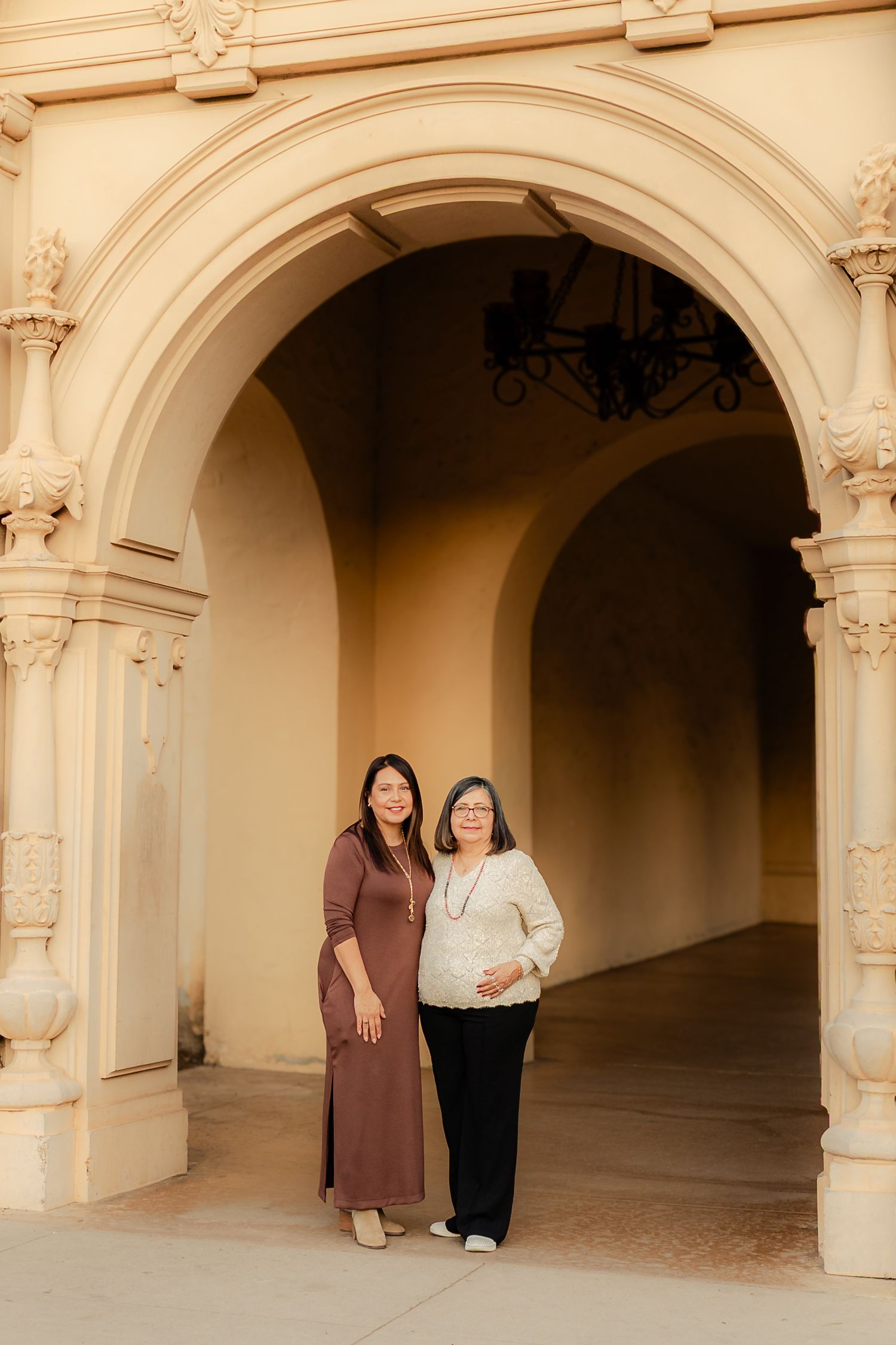 People standing in front of ornate arched walkways with beige stone columns and architectural details at historic location.