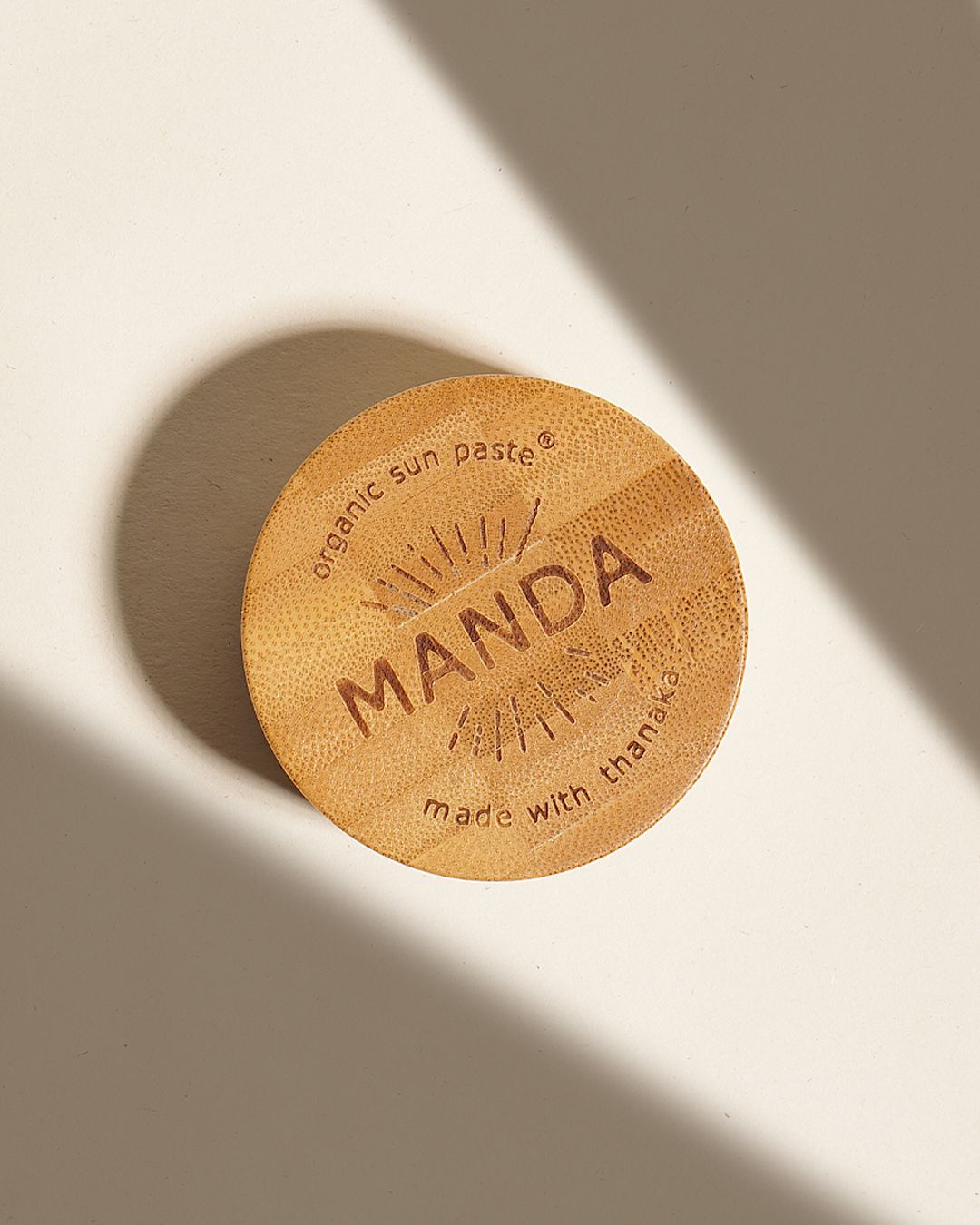 Wooden Manda branded circular discs photographed with dramatic shadows on beige background.