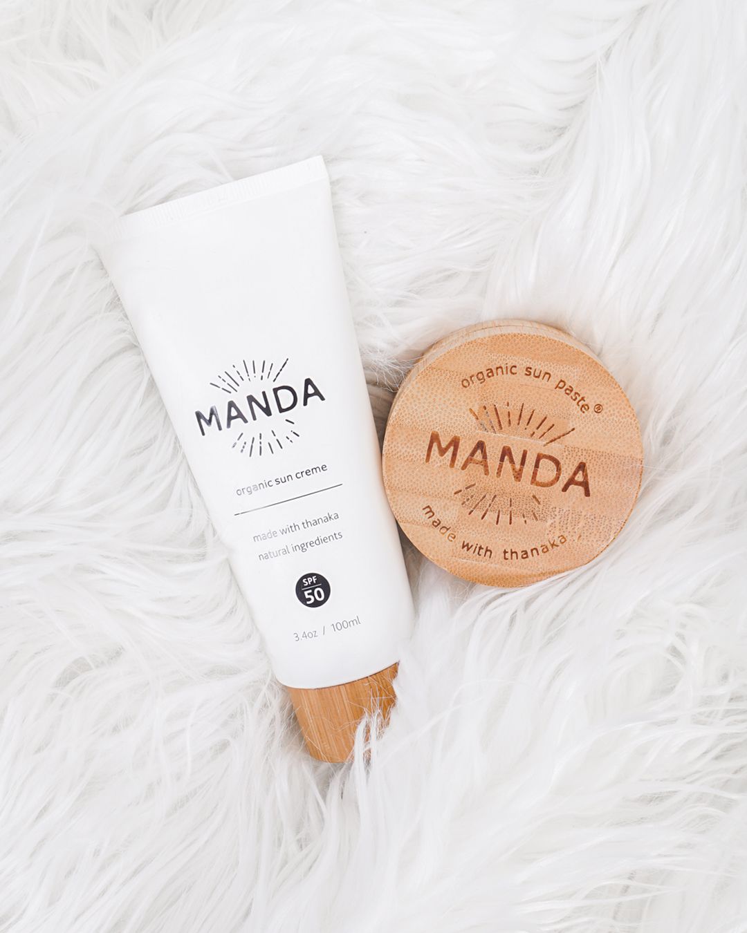 Manda organic skincare products and wooden branded items arranged on white furry background.