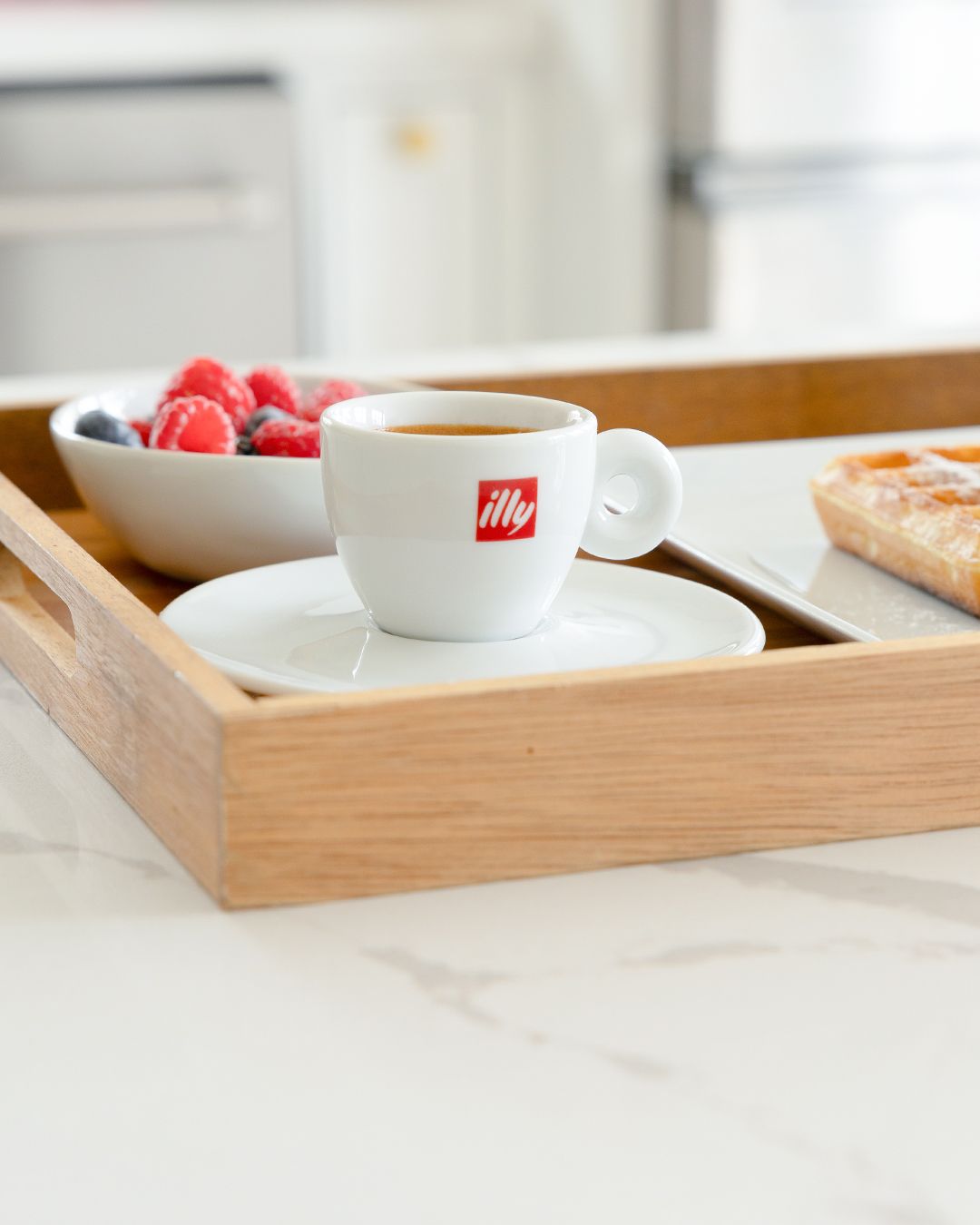 White illy coffee cup and saucer on wooden tray with raspberries and toast.