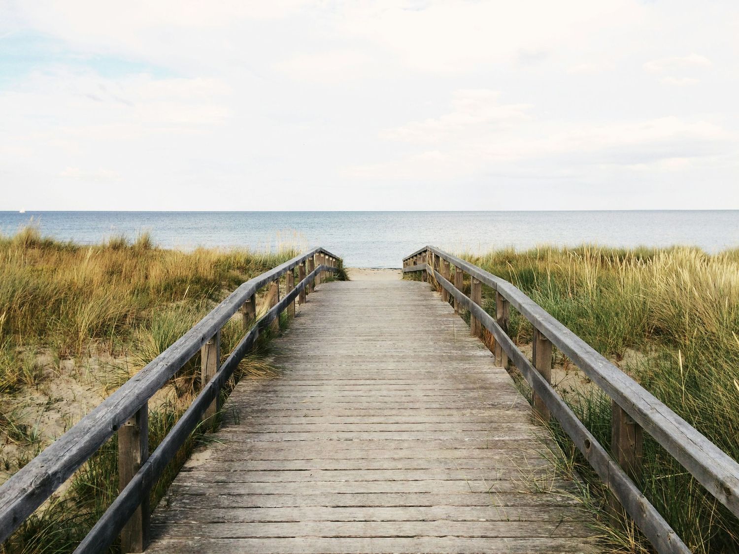 Wooden boardwalk through coastal dunes leading to ocean horizon.