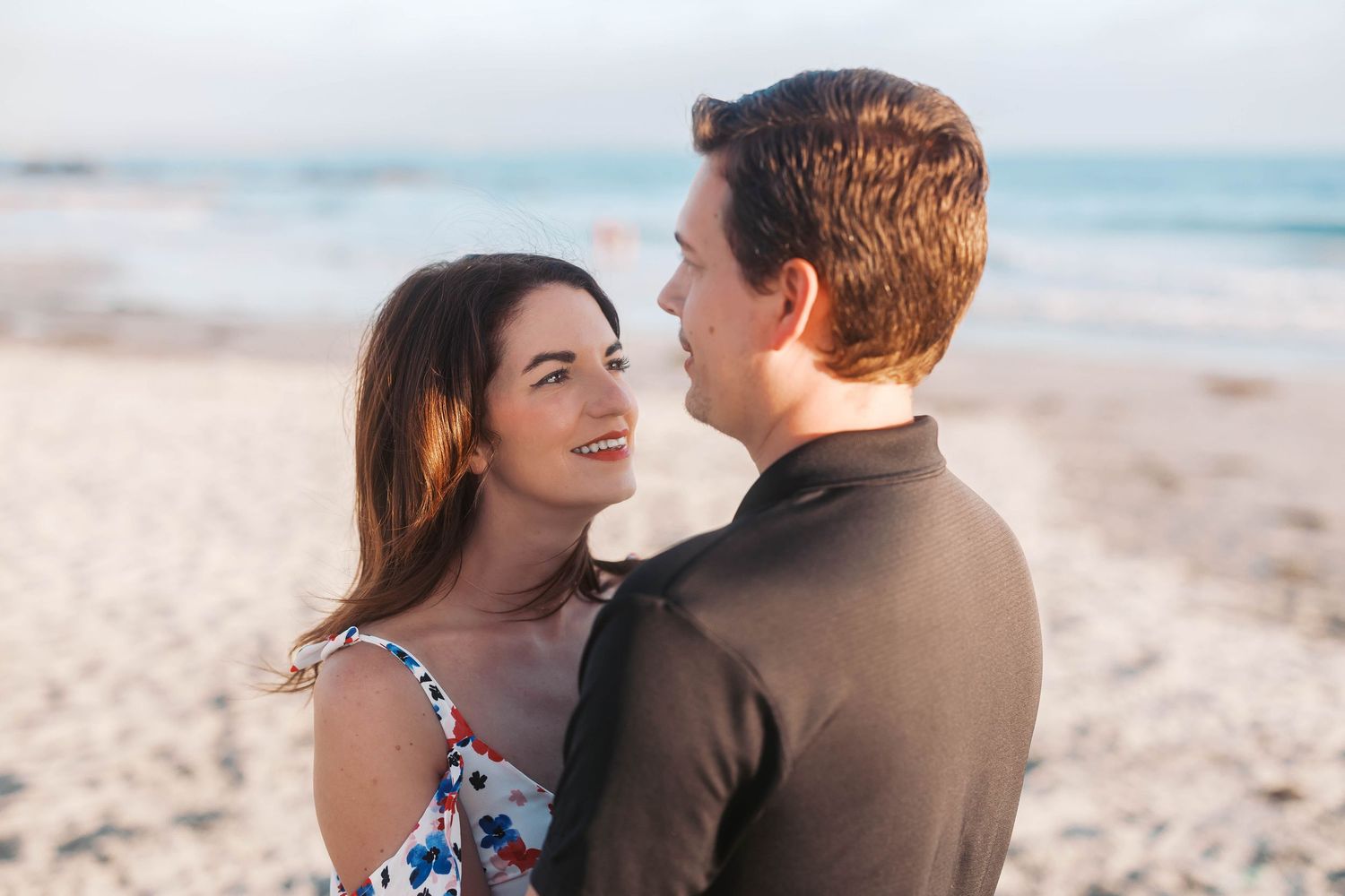 Sweet couple embracing and laughing together on a sandy beach at sunset.