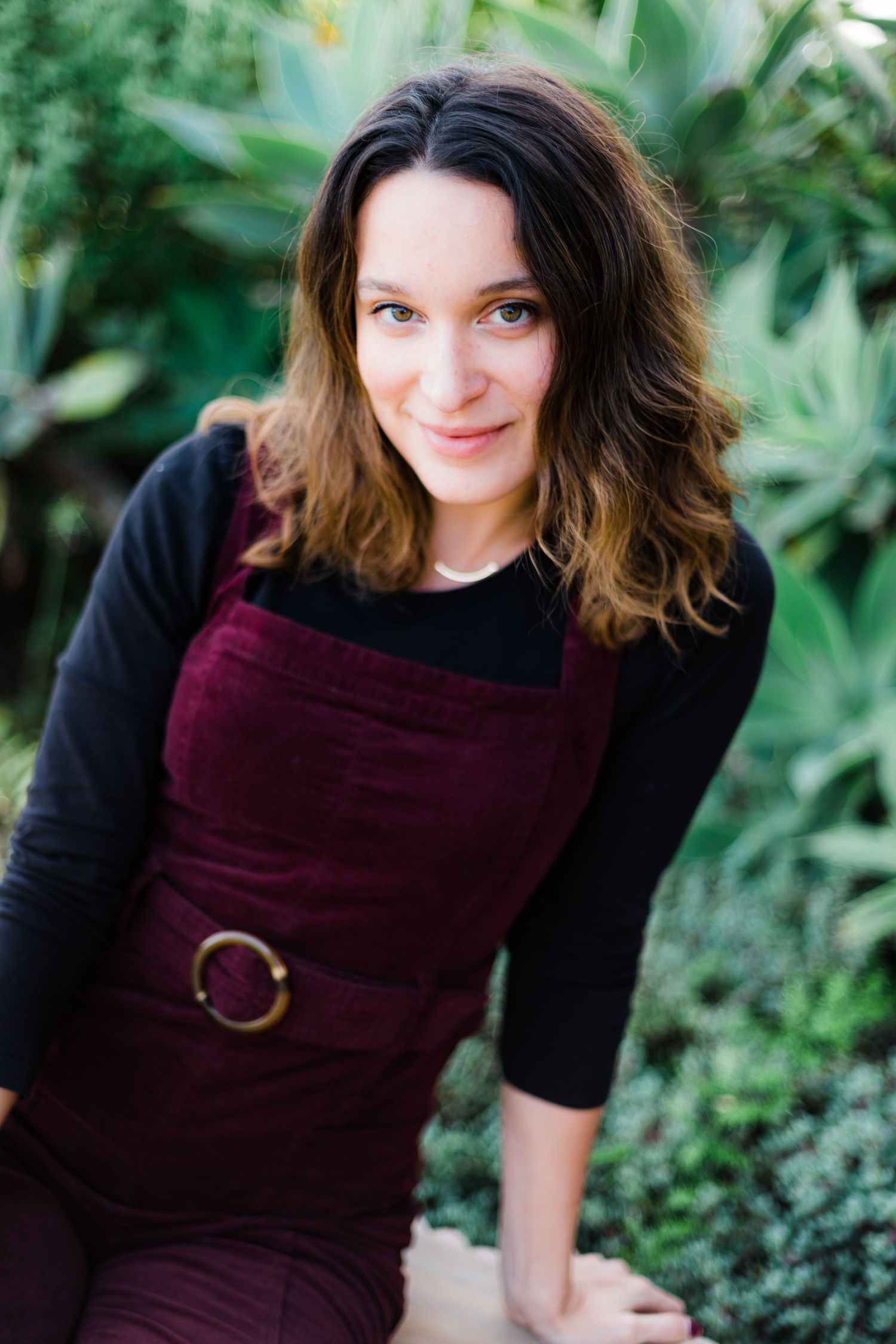 Lifestyle portraits in a garden setting wearing a burgundy dress with black sleeves.