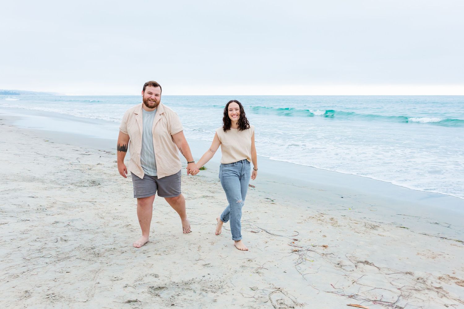 A couple runs playfully along the shoreline during a beach photoshoot.