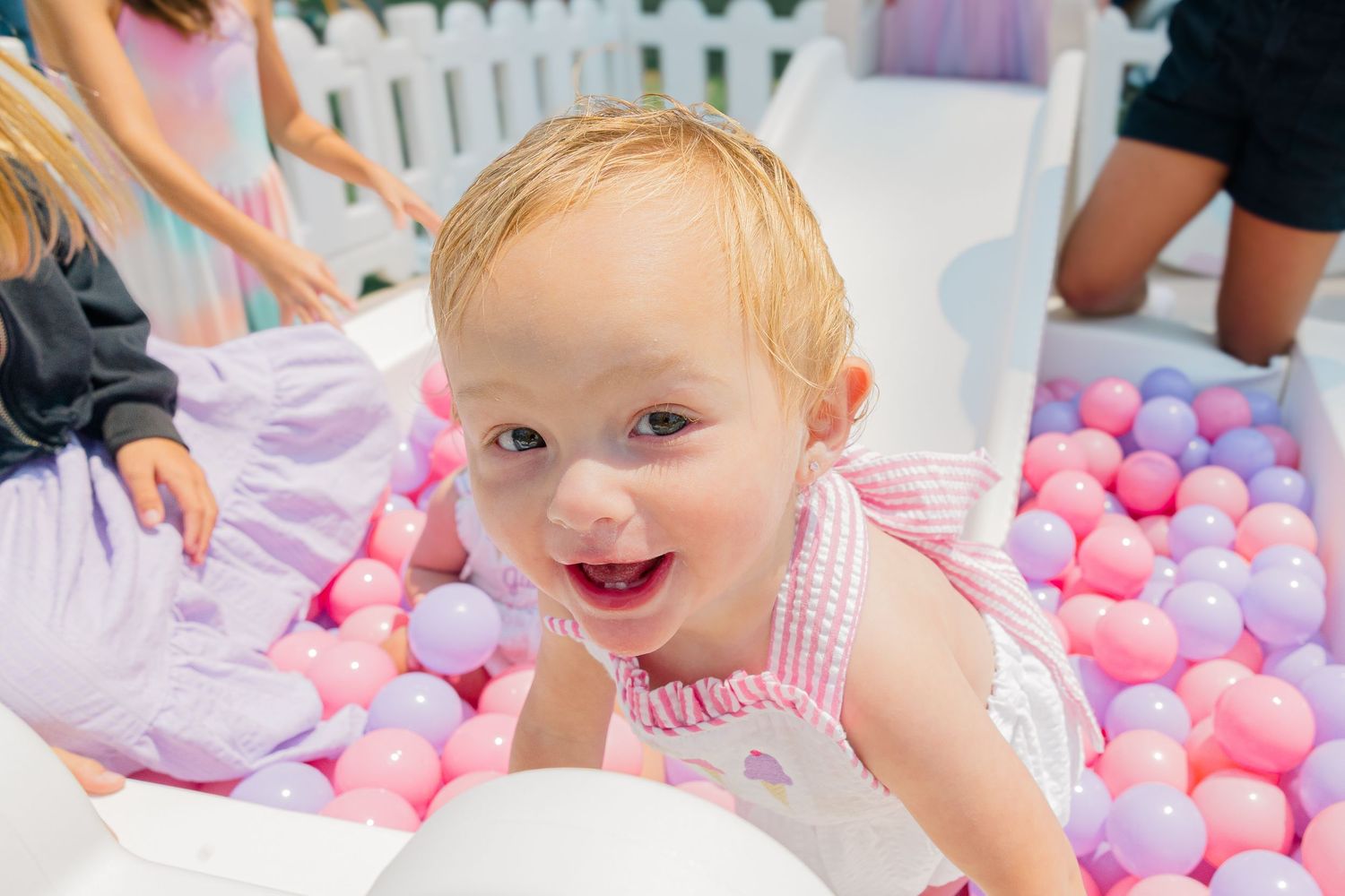Child playing joyfully in a ball pit filled with pink and white plastic balls.