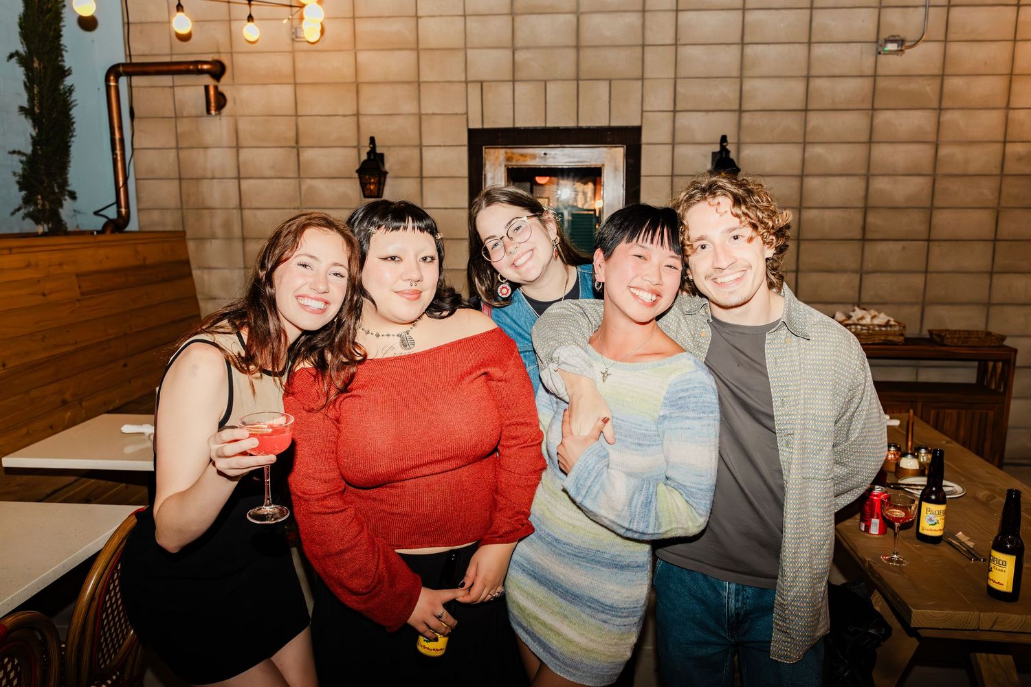 A group enjoying drinks and laughter at a casual indoor gathering with ambient lighting.