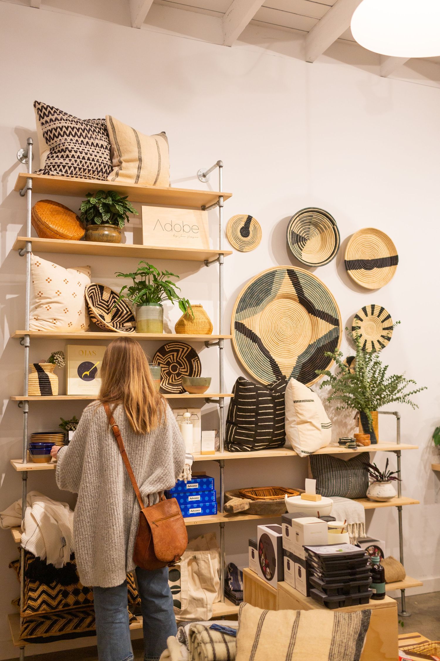 Customer browses handmade home decor items and woven baskets displayed on wooden shelves in a boutique retail store.
