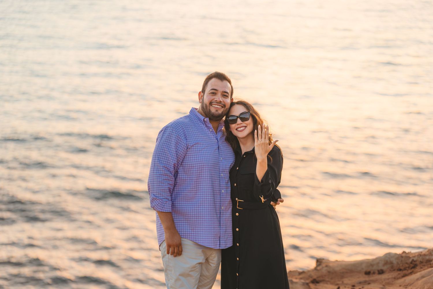 A couple enjoys a tender moment together on coastal cliffs during a beautiful sunset.