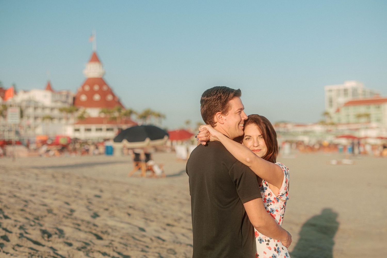 Couple enjoying a romantic moment on Coronado Beach with the historic hotel visible in the distance.